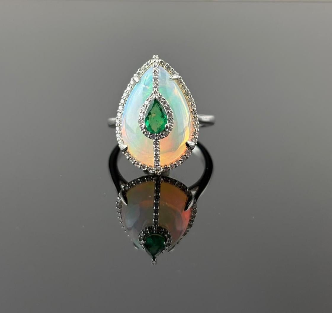 This 18K White Gold Opal, Emerald, and Diamond Ring is breathtaking . Crafted in precious 18K white gold ( 6.53 grams ) , this masterpiece showcases pear-shaped cabochon opal ( 6.94 carats ) , radiating ethereal flashes of color with every movement.