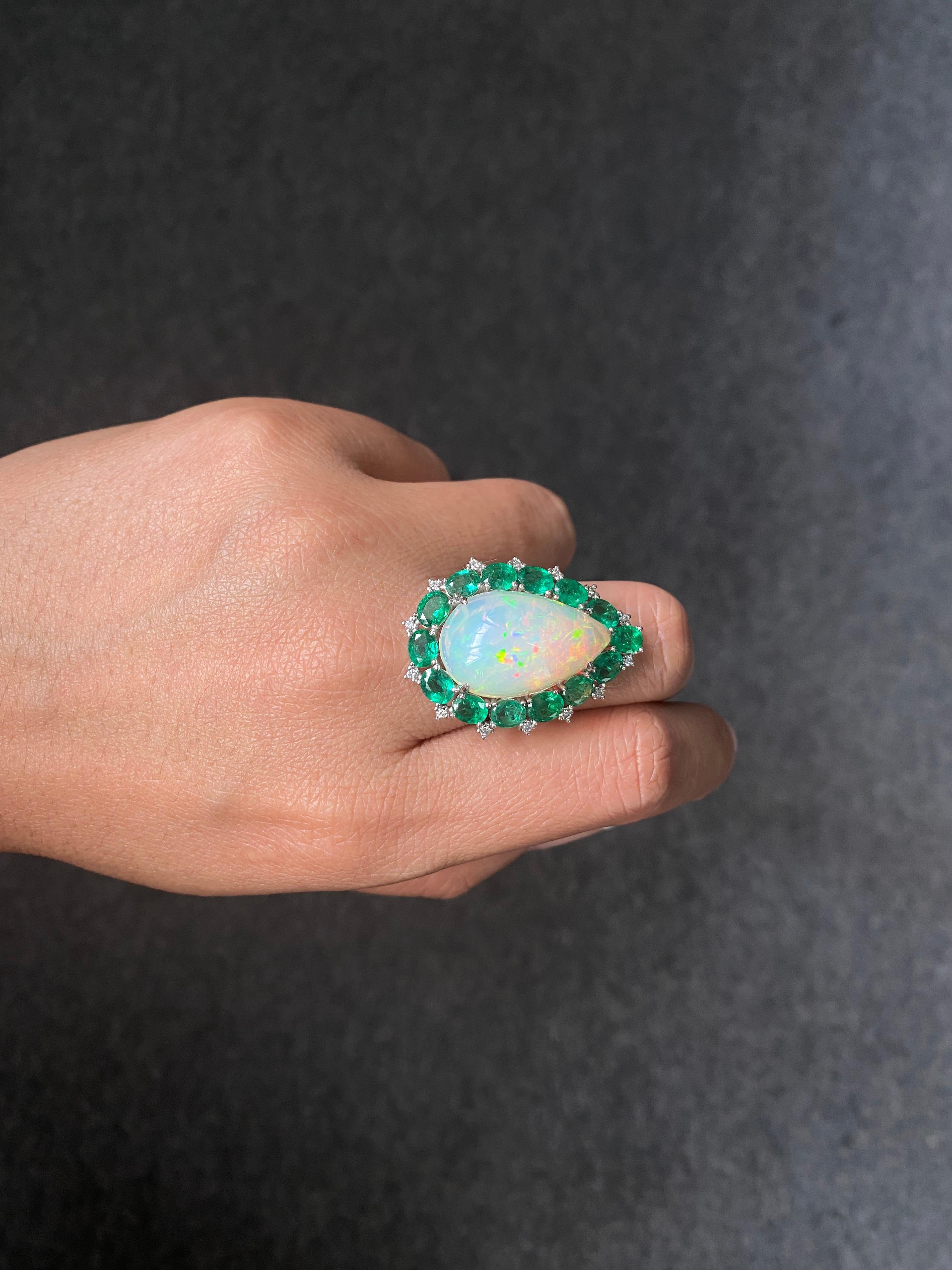 Crafted in 18K white gold, At the heart of this ring lies a breathtaking natural Opal in a pear-shaped cabochon cut ( 10.73 carats ), exuding mesmerizing flashes of color. Surrounding the opal are 14 vivid emerald ovals , creating a vibrant halo of
