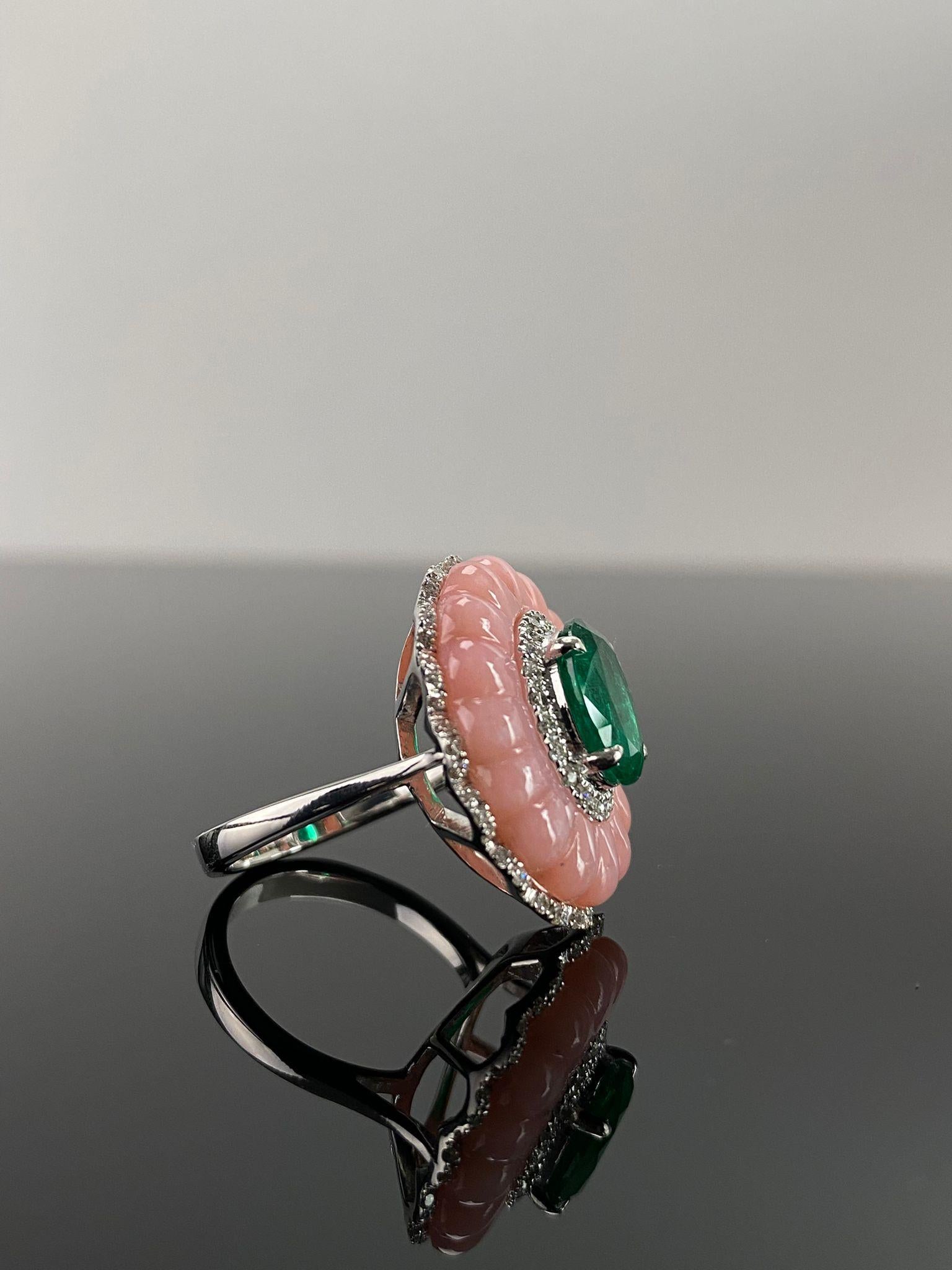 This certified ring features a rare, natural Colombian emerald in an oval cut, measuring 10.5 x 8.5 mm and weighing 2.47 carats. Encircling the emerald is an intricately carved pink opal, totaling 7.21 grams. Its soft pink color adds a delicate