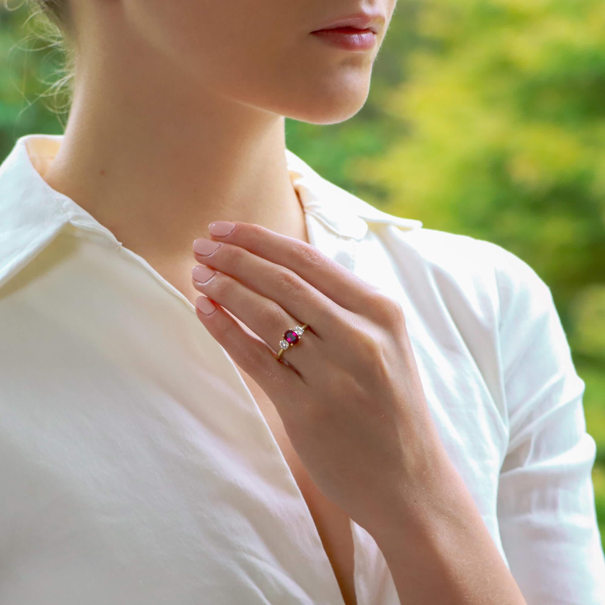 A beautiful ruby and diamond trilogy engagement ring set in 18k yellow gold. 

This classic engagement ring design is centrally set with a stunning oval cut vibrant ruby and is four claw set in an open back triple setting. The beautiful ruby is then