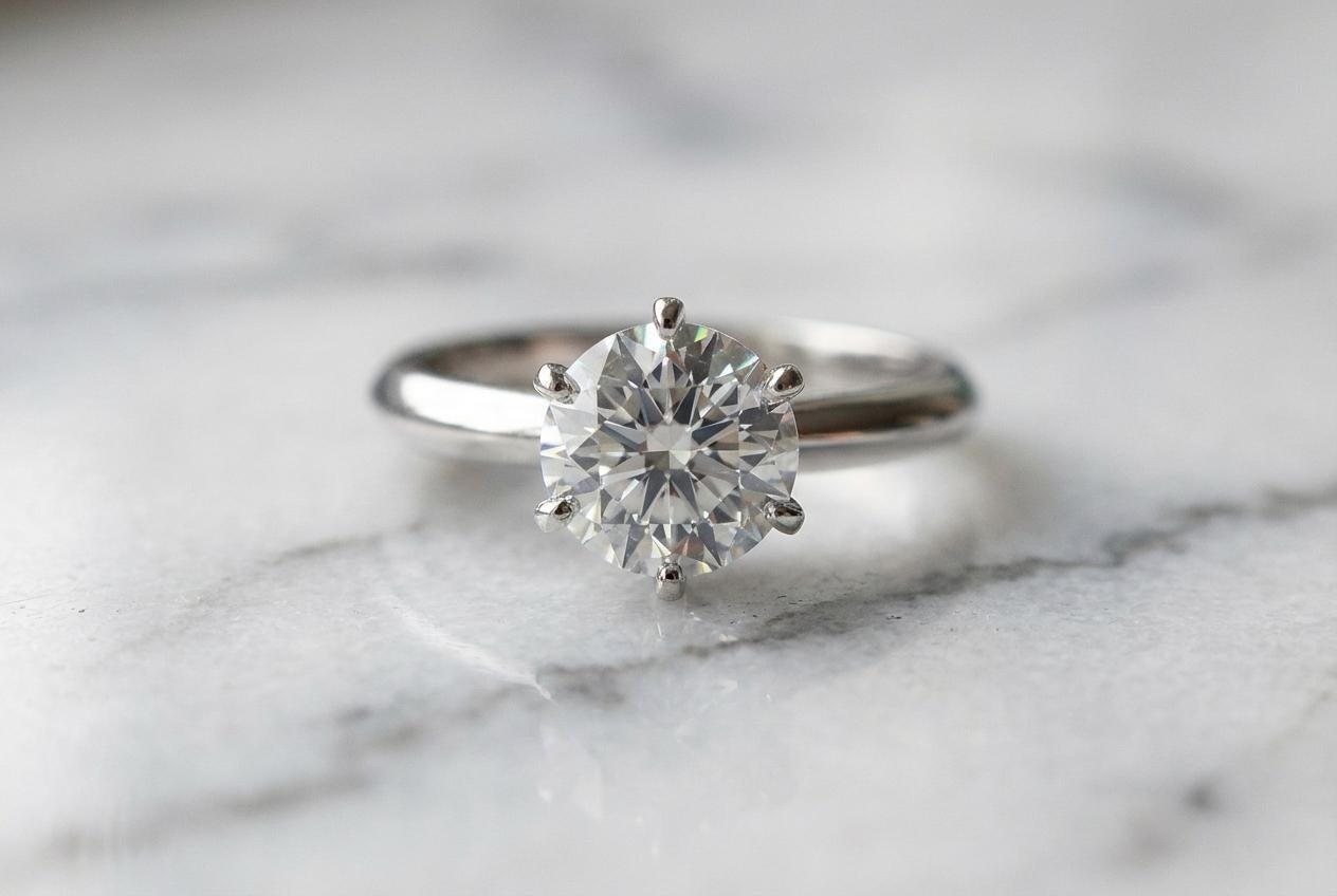 Cette bague de fiançailles en platine certifiée Tiffany & Co. est ornée d'un magnifique diamant rond brillant de 1,70 carat, méticuleusement sélectionné pour sa qualité et son éclat exceptionnels. Classé de couleur D, le diamant se situe tout en