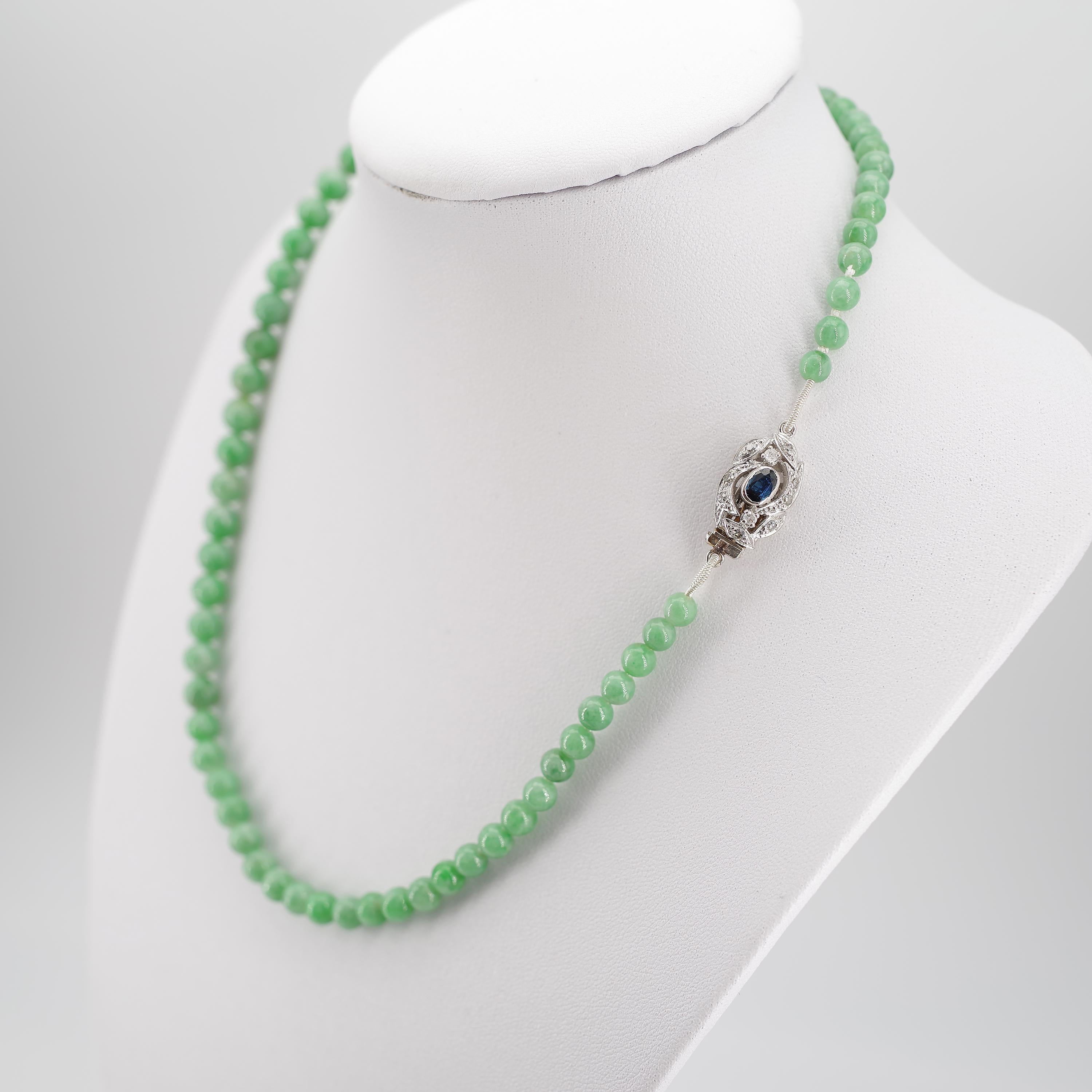 This refreshing, bright minty green jadeite jade necklace from the Art Deco era is just sixteen inches in length and features an elegant clasp of 18K white gold centered with a gemmy little natural oval cut sapphire of about one-quarter carat. Small