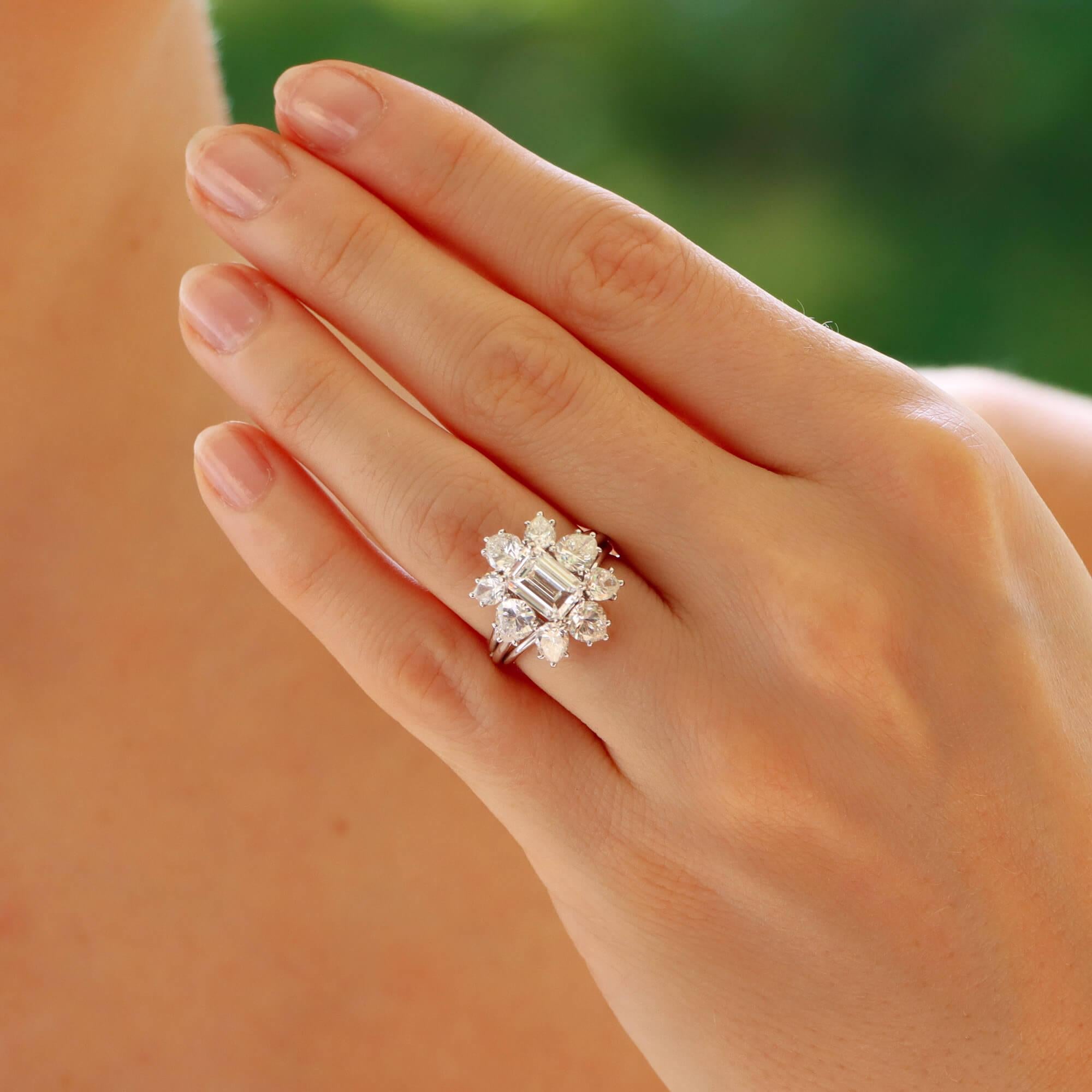 A beautiful certified vintage Cartier emerald cut cluster ring set in platinum.

The piece is predominately set with a sparkly certified D-colour emerald cut diamond which is securely four claw set amongst a cluster of pear cut diamonds. The pear