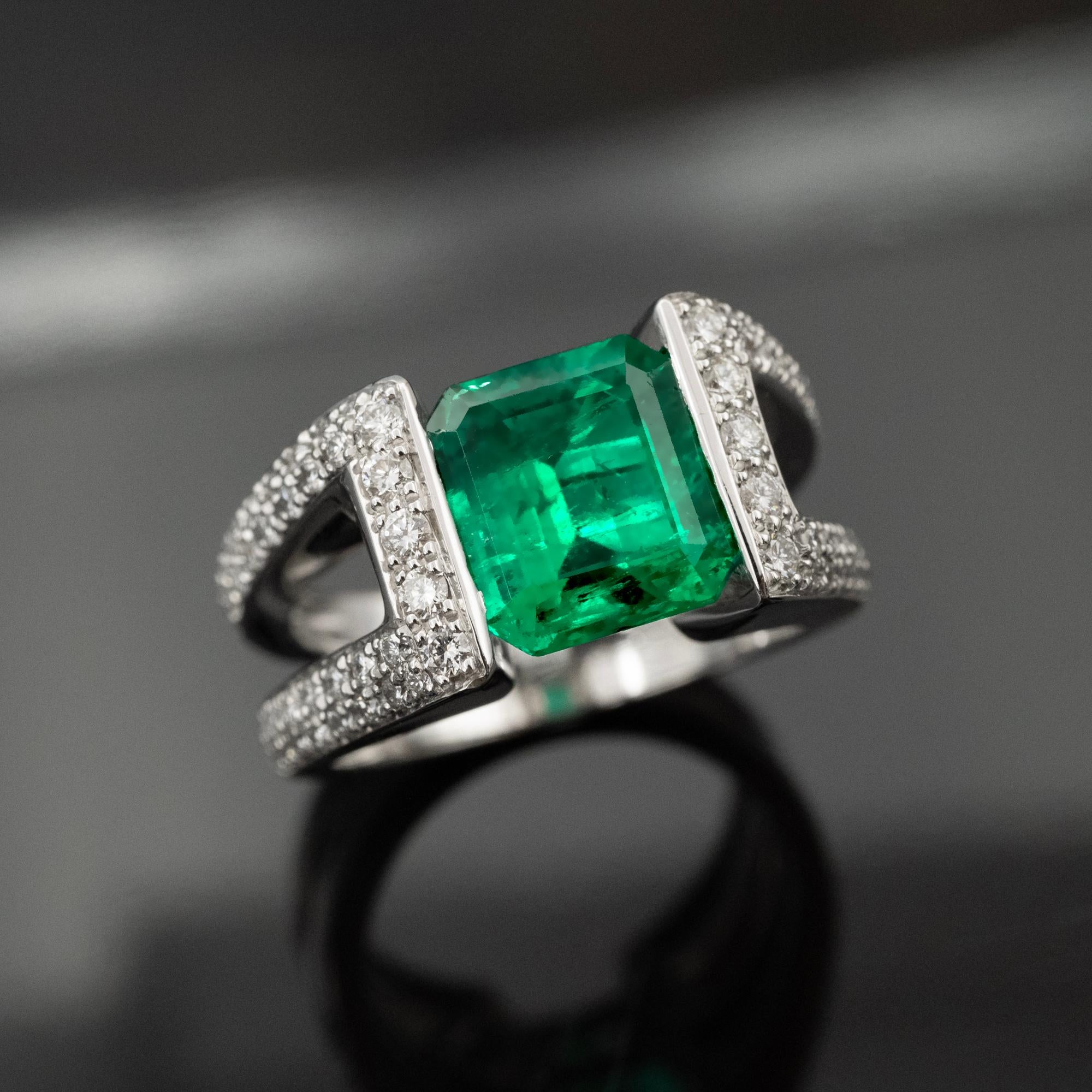 This 18-karat white gold engagement ring is a striking embodiment of classic allure harmoniously blended with modern sophistication. 
At its heart lies a captivating Colombian emerald of 2.58 carats. Its provenance is authenticated by a certificate