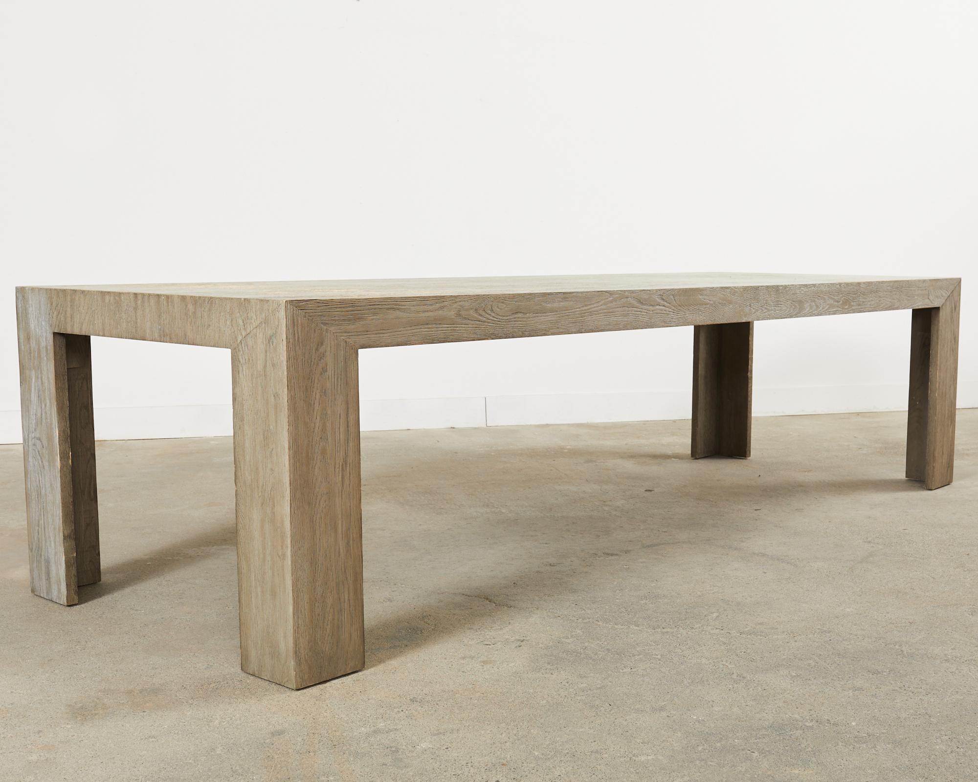 Monumental rectangular dining table measuring 10 feet long featuring an oak veneer with a distressed, cerused stained finish. The table was designed in the parsons style with modern bracket legs. Excellent joinery and craftsmanship that seats up to