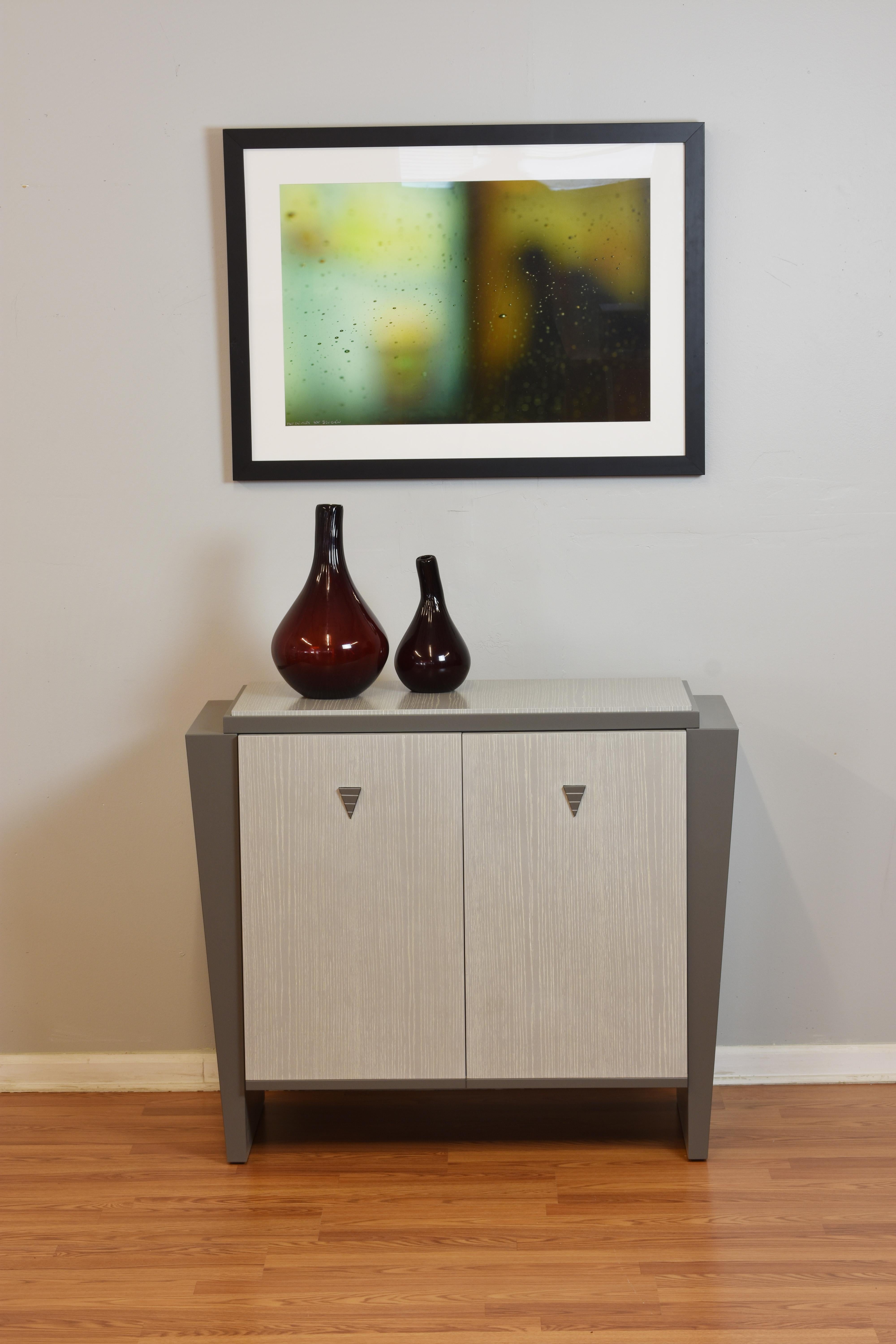This Diva buffet and storage accent cabinet is shown with Cerused Facade and top with grey lacquered legs and detailing. It has two silverware drawers lined with anti tarnish felt lineer. Adjustable shelves.

All our work is signed and dated and