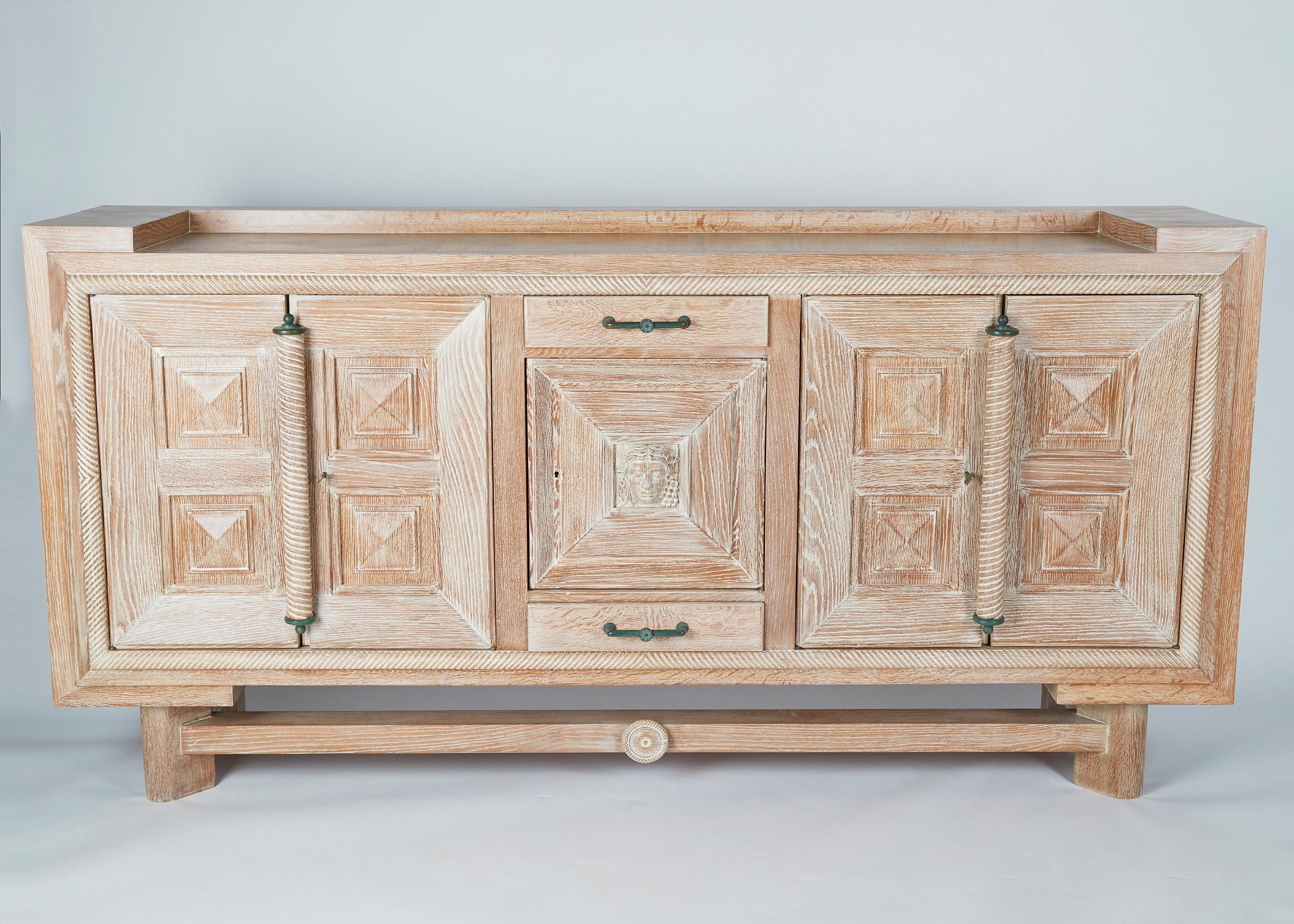 This impressive cabinet in Cerused wood possesses elements characteristic of France's late Art Deco aesthetic. Extraordinary for its size and carved details, including the classically inspired emblem centered in the cabinet's facade, and the