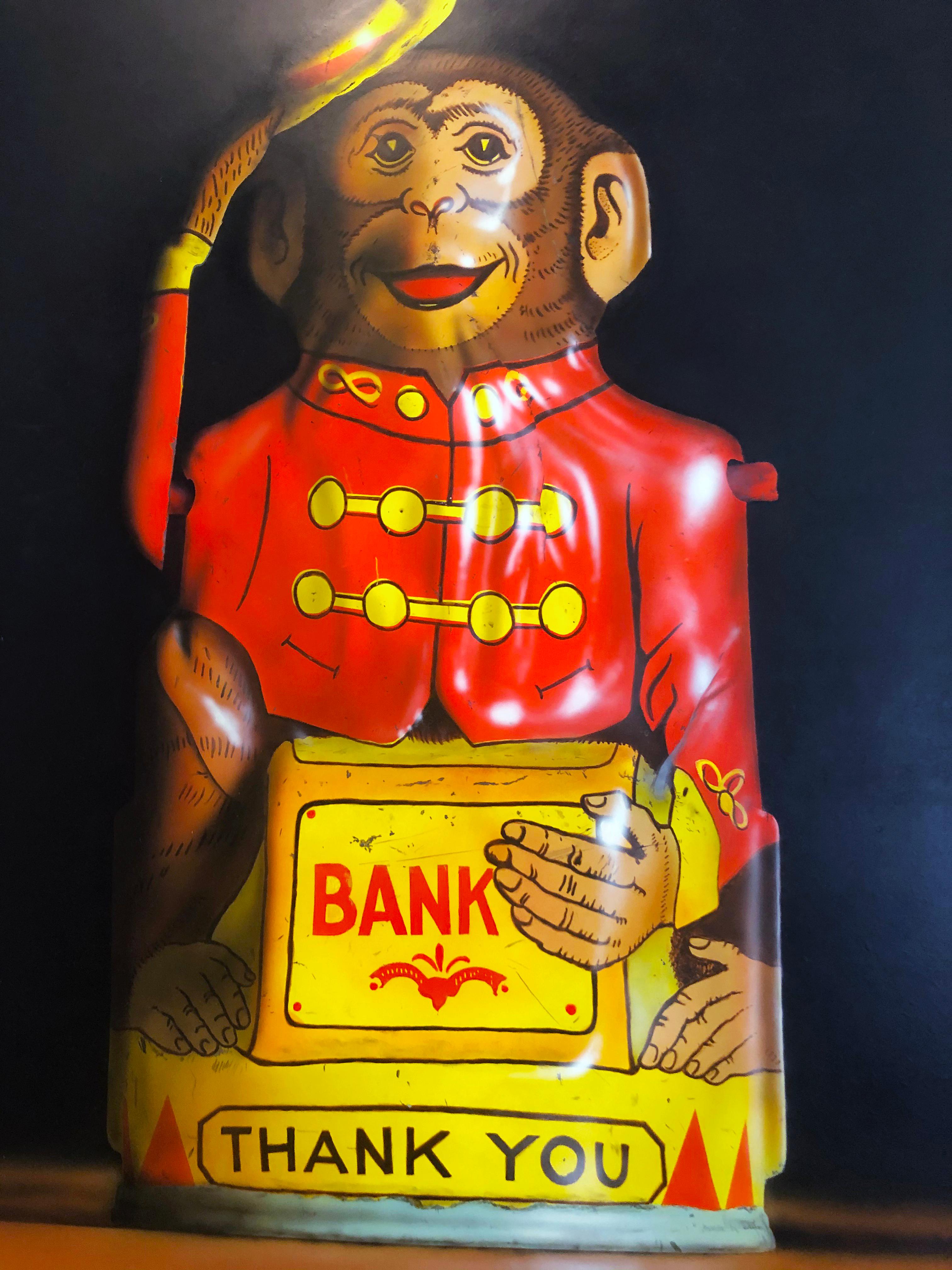 'Two Toy Banks' 1982 by American artist Cesar J. Santander. Oil on panel, 27.75 x 34.5 in. This painting features a finely detailed monkey and clown piggy banks rendered in rich colors of red, yellow, blue, brown and black. Framed in a gold