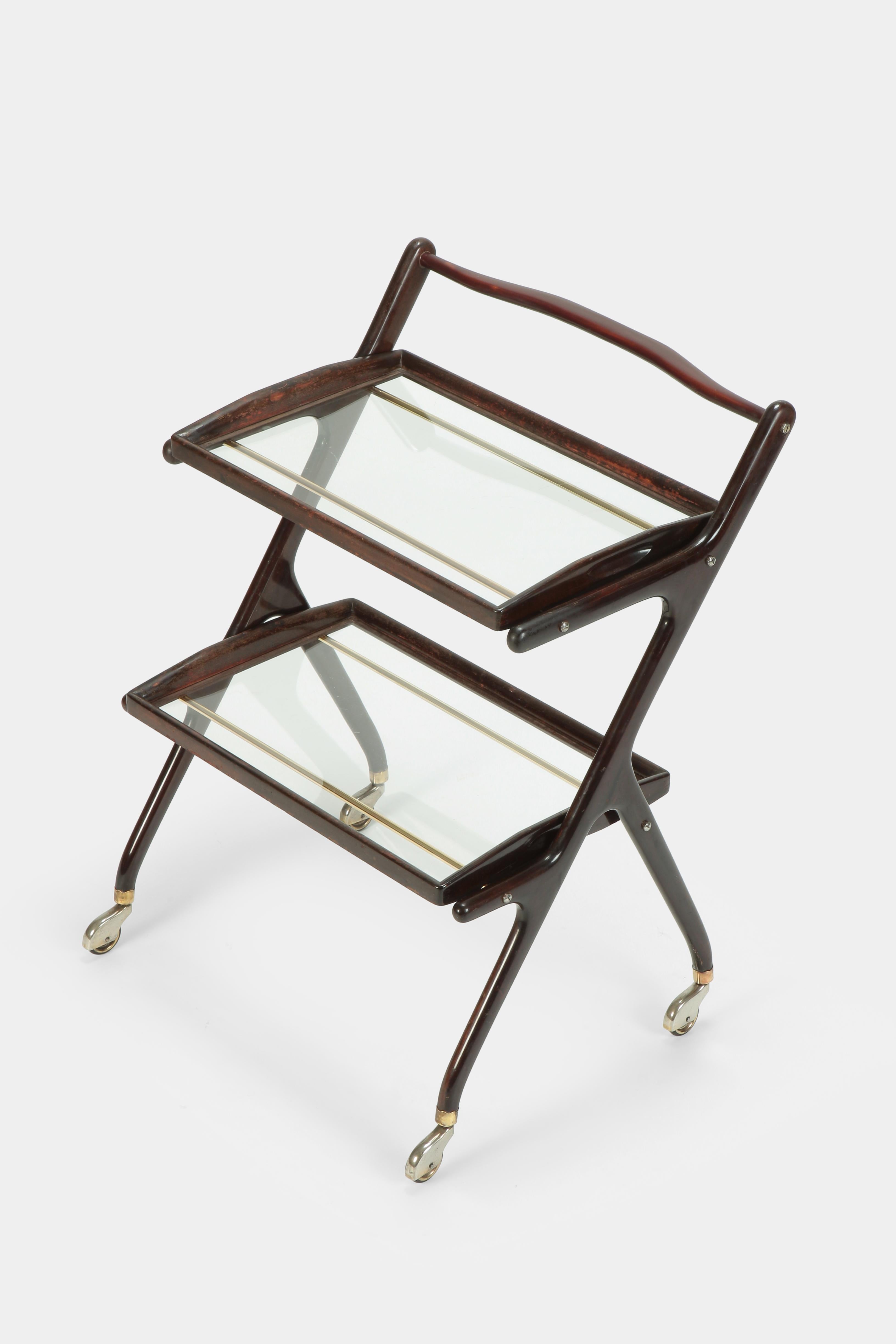 Cesare Lacca bar cart manufactured in the 1950s in Italy. The frame is made of solid mahogany wood. Two dismountable serving trays with glass surrounded by mahogany placed on two brass braces.