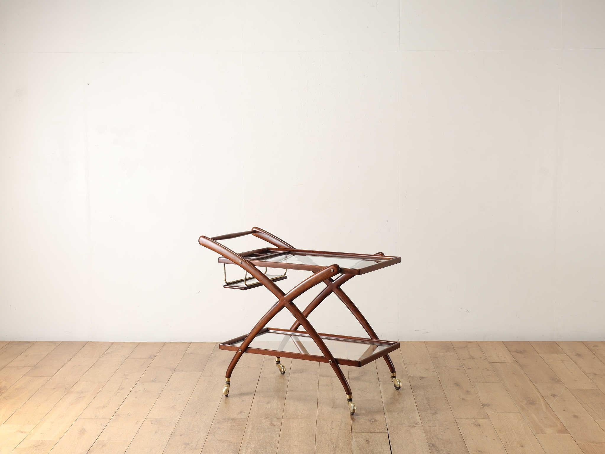 This tea cart was designed by CESARE LACCA, an Italian architect and designer born in Naples. The wood frame gives it a nostalgic warmth, making it easy to fit into any space. The crossed legs and the use of glass for the top panel give it a light