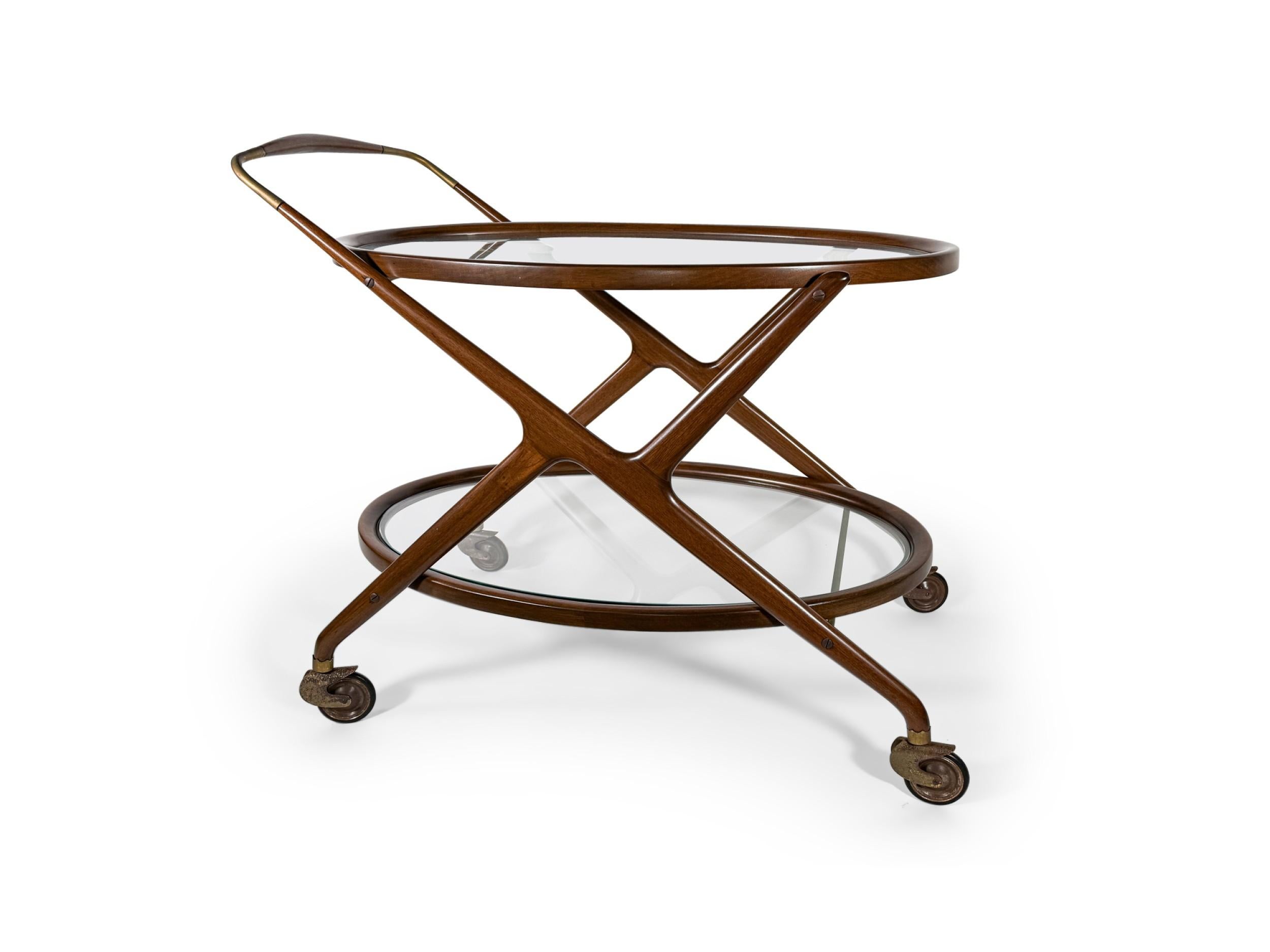 Carro de servir/carro de té italiano de mediados de siglo, de forma ovalada, con armazón de teca teñida de oscuro, dos estantes de cristal insertados y asa y varillas de soporte de latón, apoyado sobre cuatro ruedas. (CESARE LACCA)