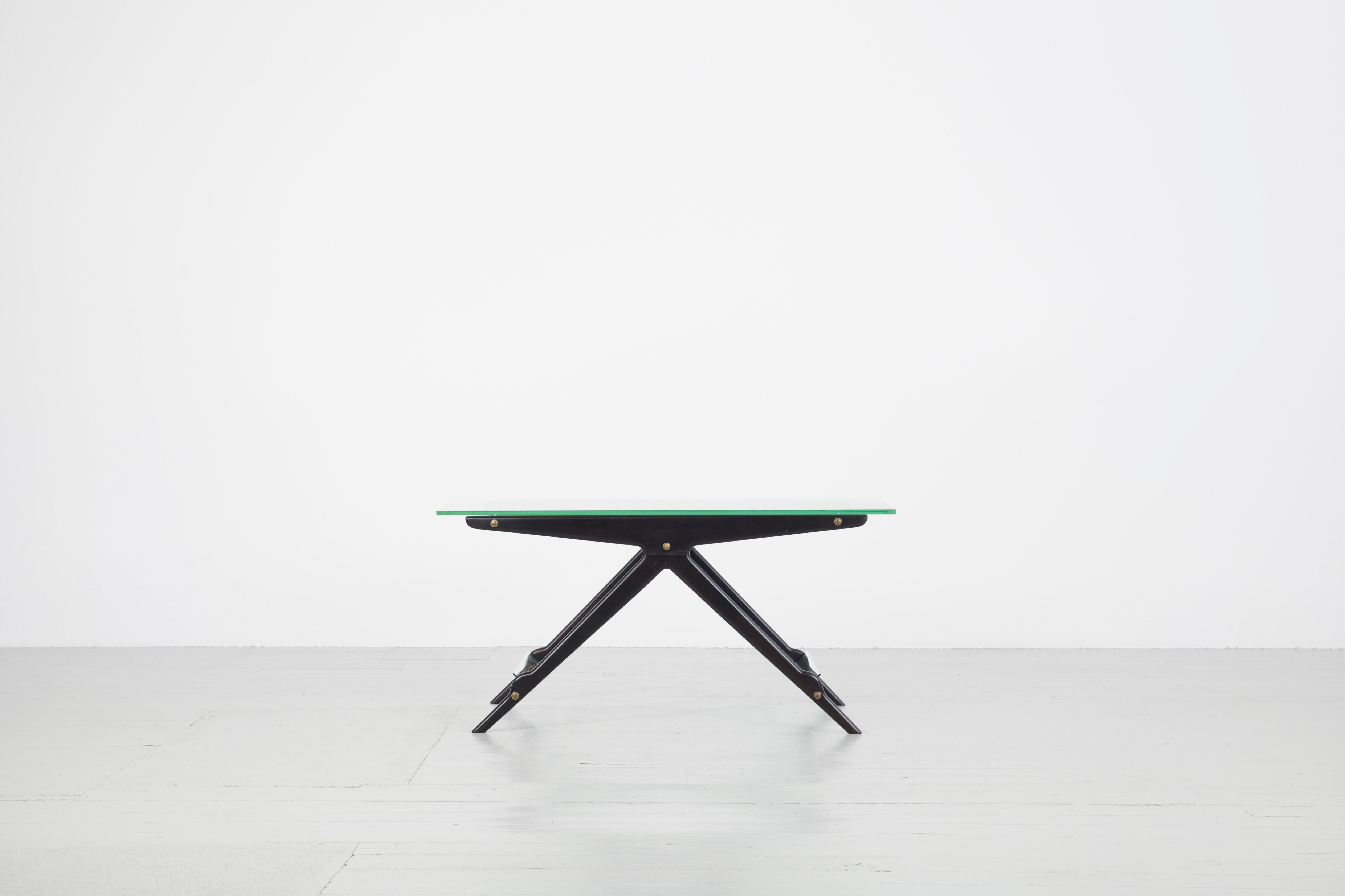 Cette table basse italienne a été conçue par Cesare Lacca dans les années 1950. Le cadre en bois laqué noir est construit en forme de T évasé. Entre les paires de pieds, des plaques de verre sont encastrées comme porte-revues. Le plateau de la table