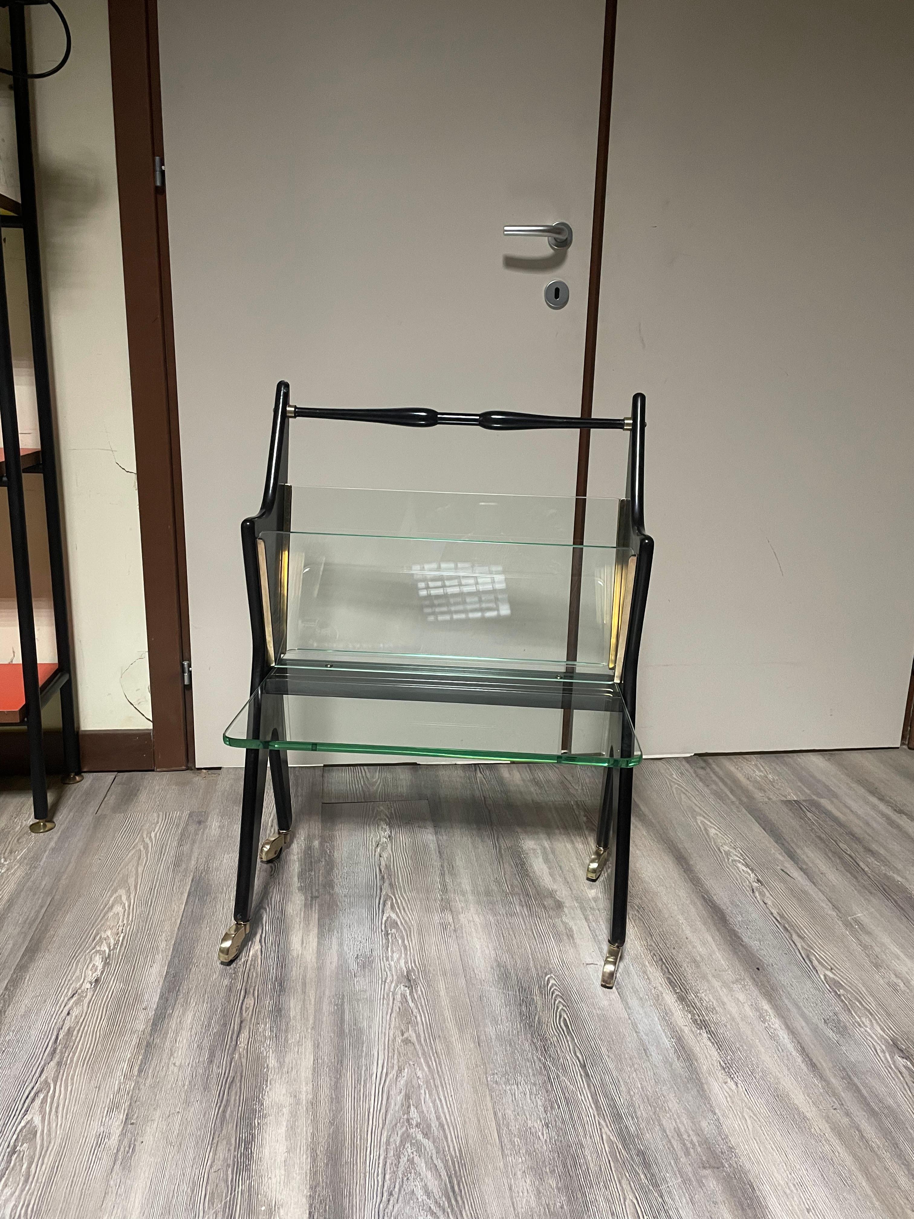 Magazine rack and side table by Cesare Lacca, 1950s. 

Stained black wooden structure, glass tops and brass details.

In perfect original condition, except for the rubbers on the wheels which have flattened and therefore do not allow them to