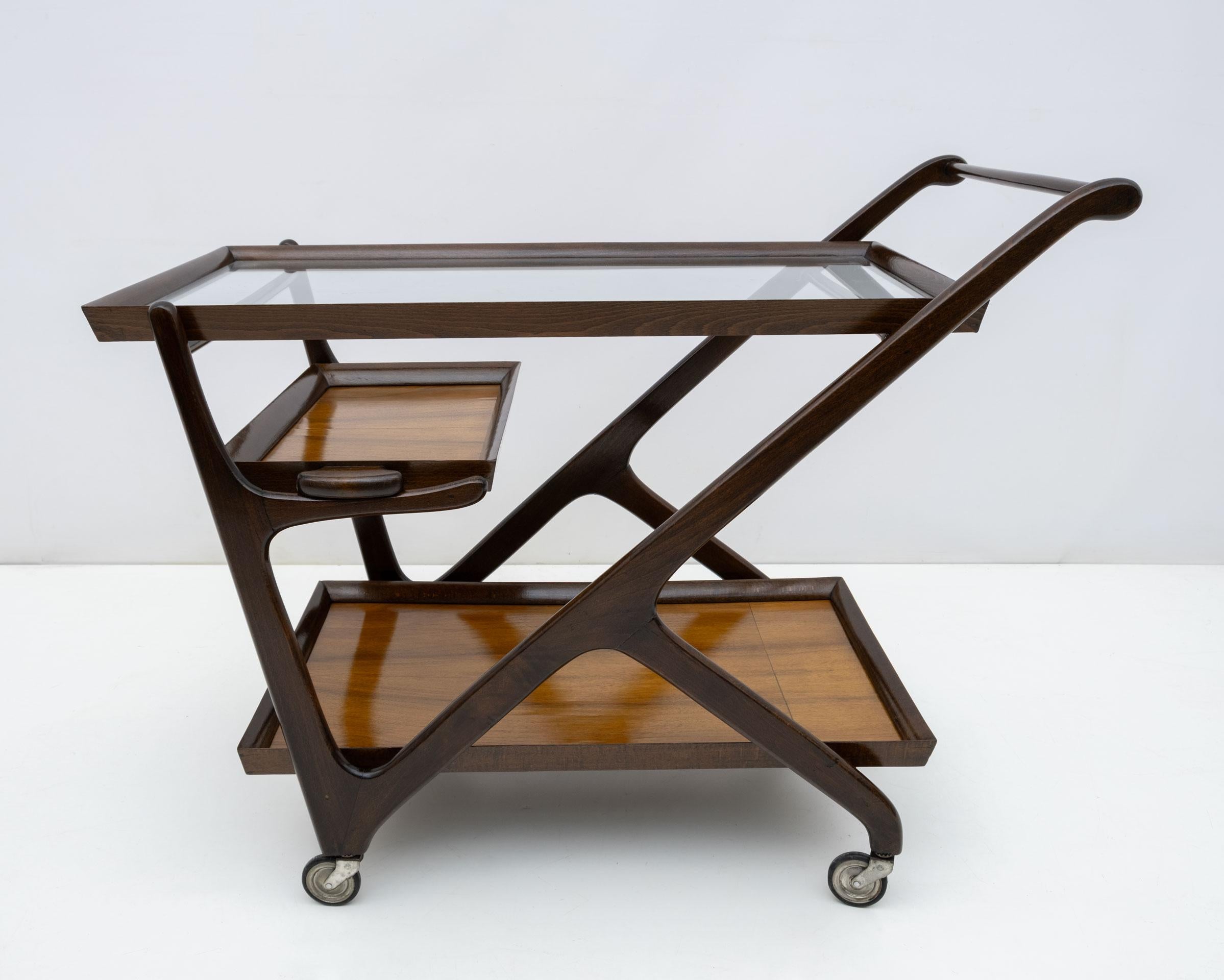 Dieser Barwagen aus Nussbaumholz wurde in den 1950er Jahren von Cesare Lacca für Cassina entworfen. Wie es das Schicksal so will, ist er mit zwei herausnehmbaren Tabletts und einer oberen, stets abnehmbaren Glasplatte ausgestattet.
Der Barwagen