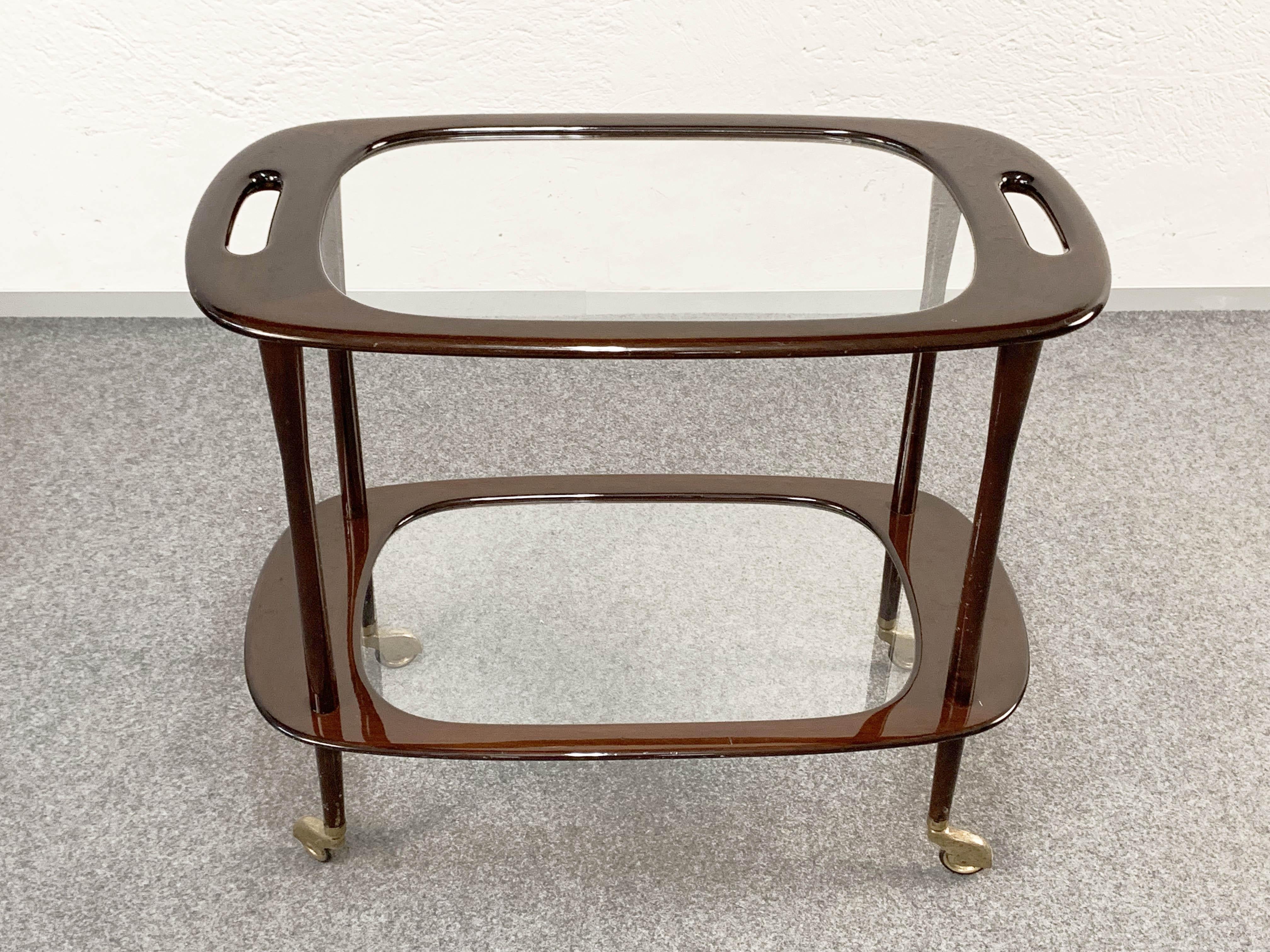 Amazing midcentury mahogany Italian serving bar cart. It was designed by Cesare Lacca for Cassina during the 1950s in Italy.

It is composed of two shelves, made of solid mahogany wood with its original crystal glass. Wheels have brass