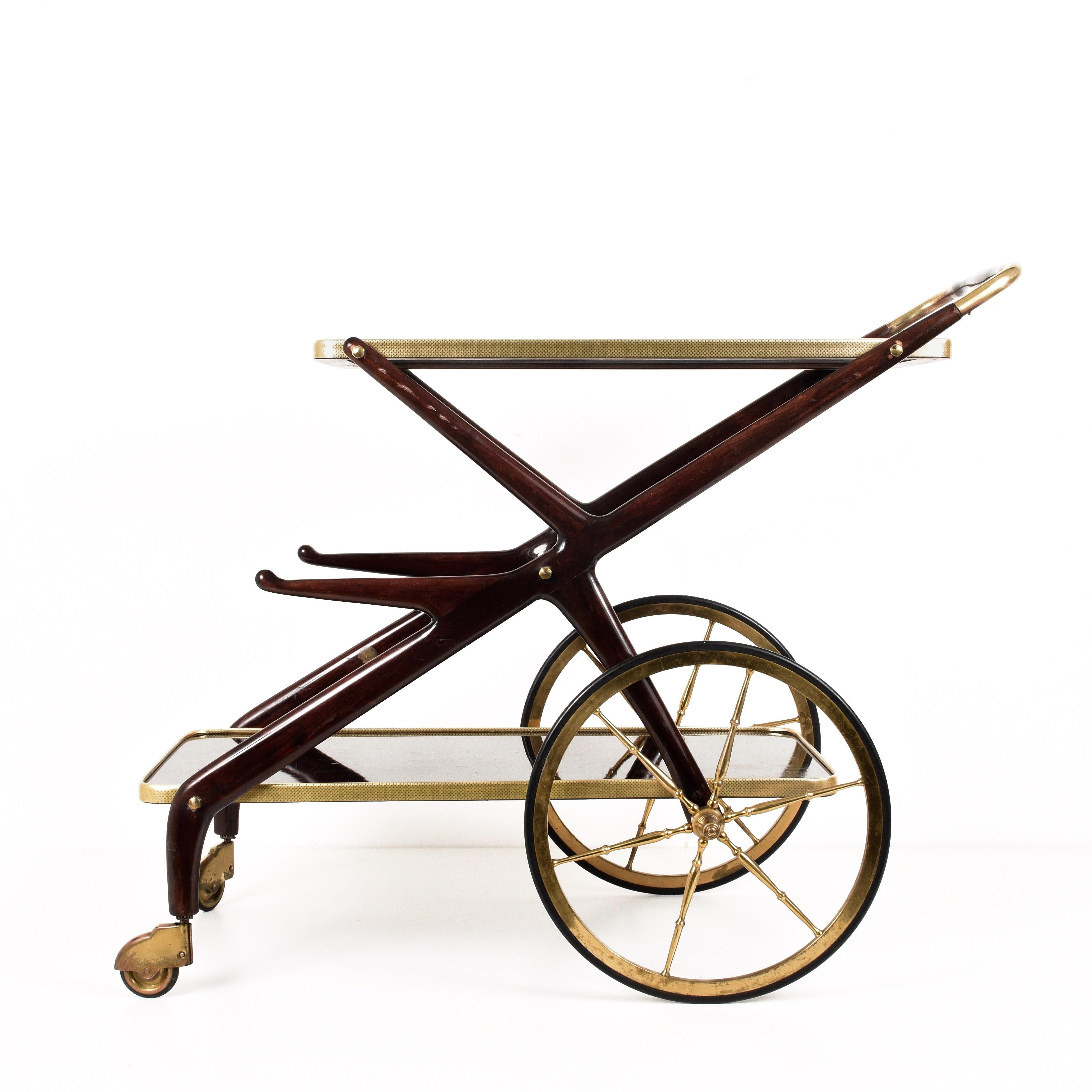Amazing bar trolley in wood with glass top and large wheels in brass. This wonderful piece was produced in Italy during the 1950s.

This astonishing bar cart features, two big wheels in brass, a sinuous wood structure vitrified with two shelves and