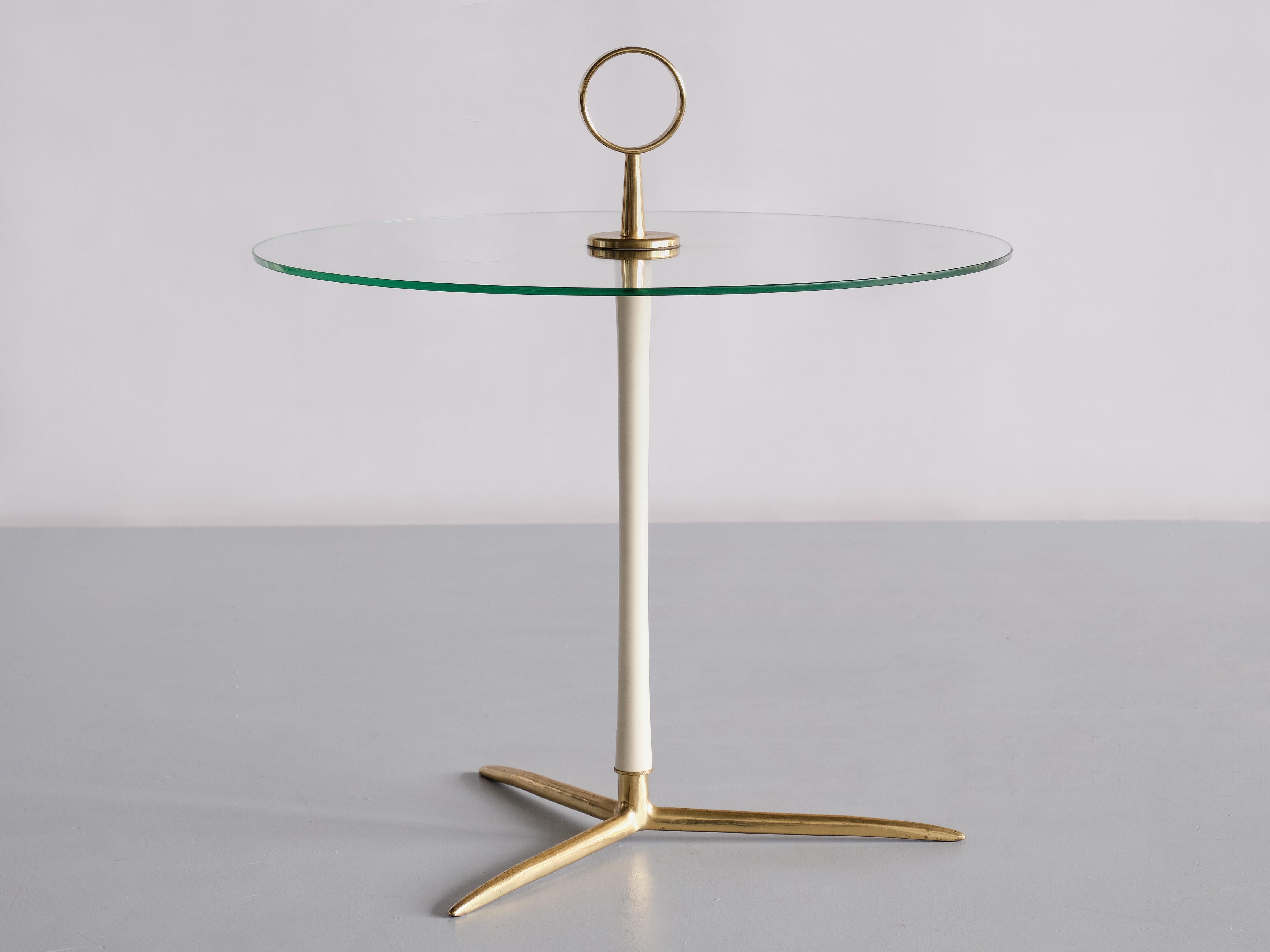This elegant side table was designed by Cesare Lacca and manufactured in Italy in the mid 1950s. The table consists of a sculptural three legged base in brass and central stem in cream white lacquered metal. The round top in hardened, glass with a