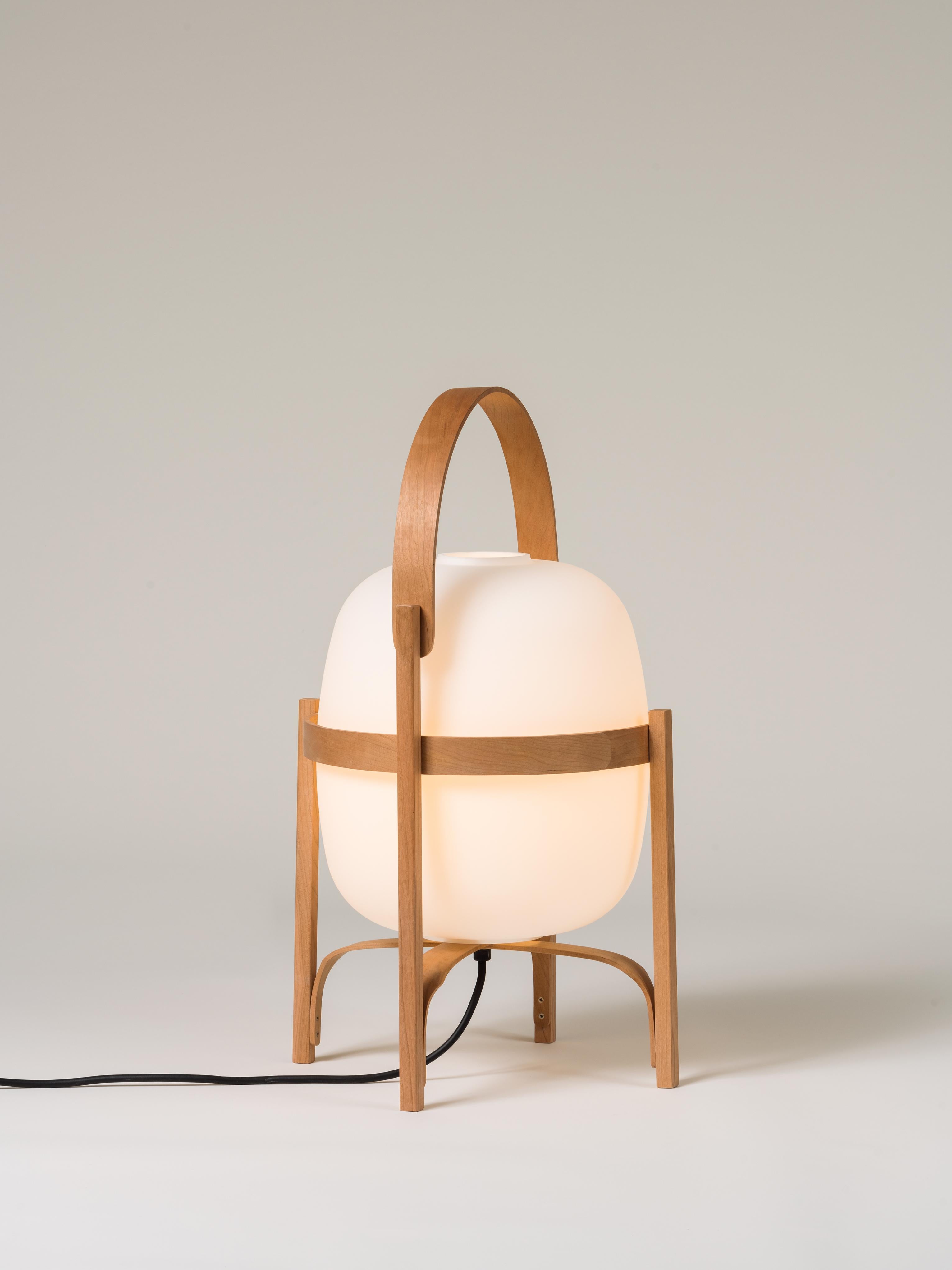 Cesta table lamp by Miguel Milá
Dimensions: D 33 x H 57 cm
Materials: Cherry wood, glass.

On a stroll through Barcelona in the 1960s, designer Miguel Milá found an abandoned opal globe outside a glass factory. He took it home, and over the