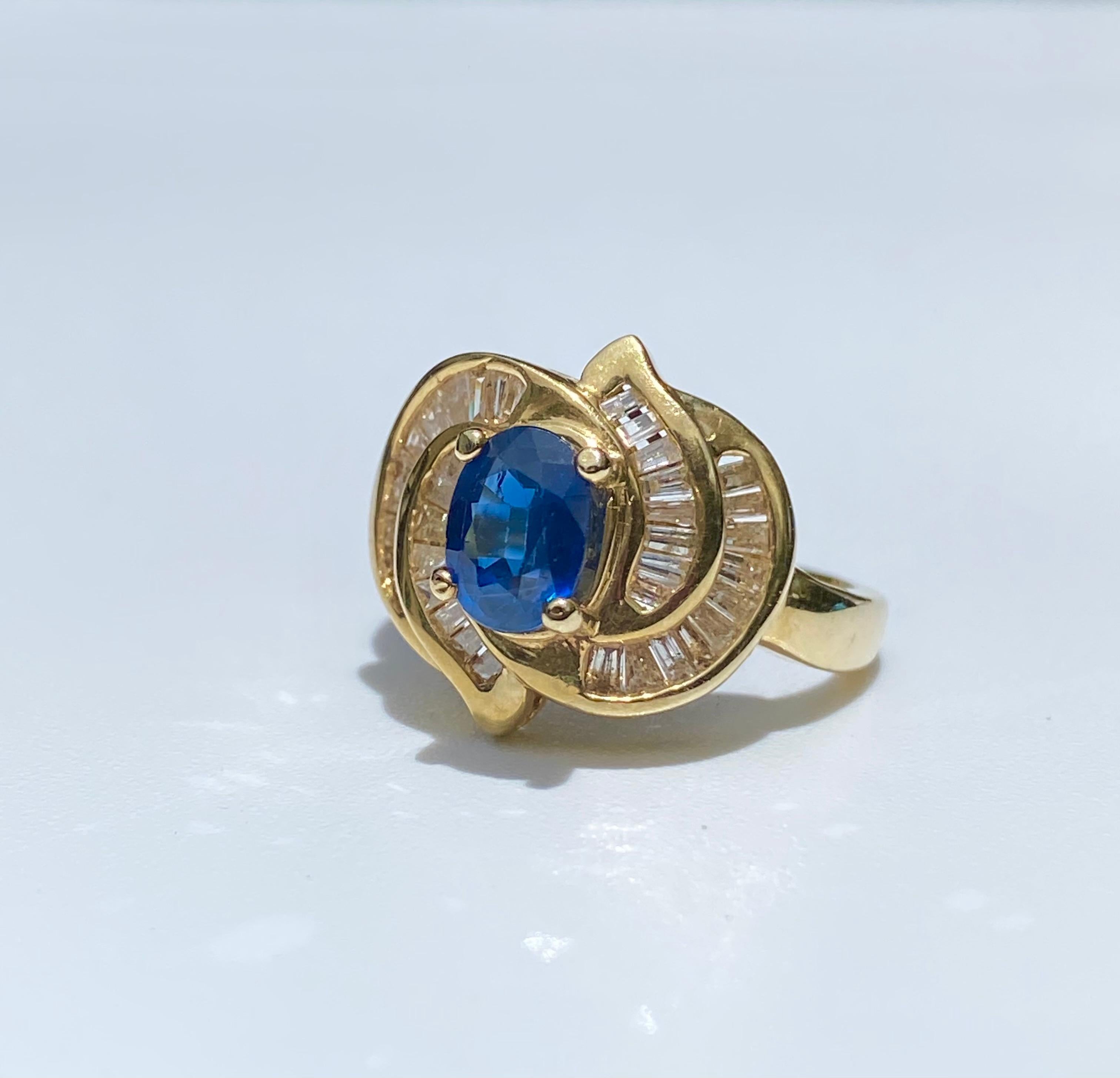 Centering a 0.89 Carat Oval-Cut Ceylon (Sri Lanka) Blue Sapphire, accented by Baguette-Cut Diamonds, and set in 14K Yellow Gold. 

Details:
✔ Center Stone: Blue Sapphire
✔ Sapphire Weight: 0.89 carats
✔ Sapphire Origin: Thailand 
✔ Sapphire Cut: