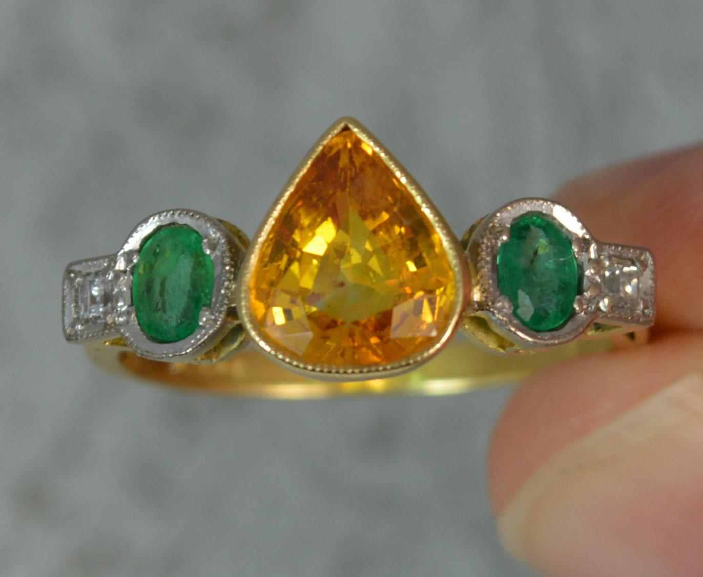 A stunning and very rare orange sapphire, emerald and diamond ring.
SIZE ; N 1/2 UK, 7 US
Modelled in 18 carat yellow gold with platinum head setting.
Designed with a pear cut Ceylon origin sapphire to the centre in bezel setting, 7.4mm x 8.8mm. To