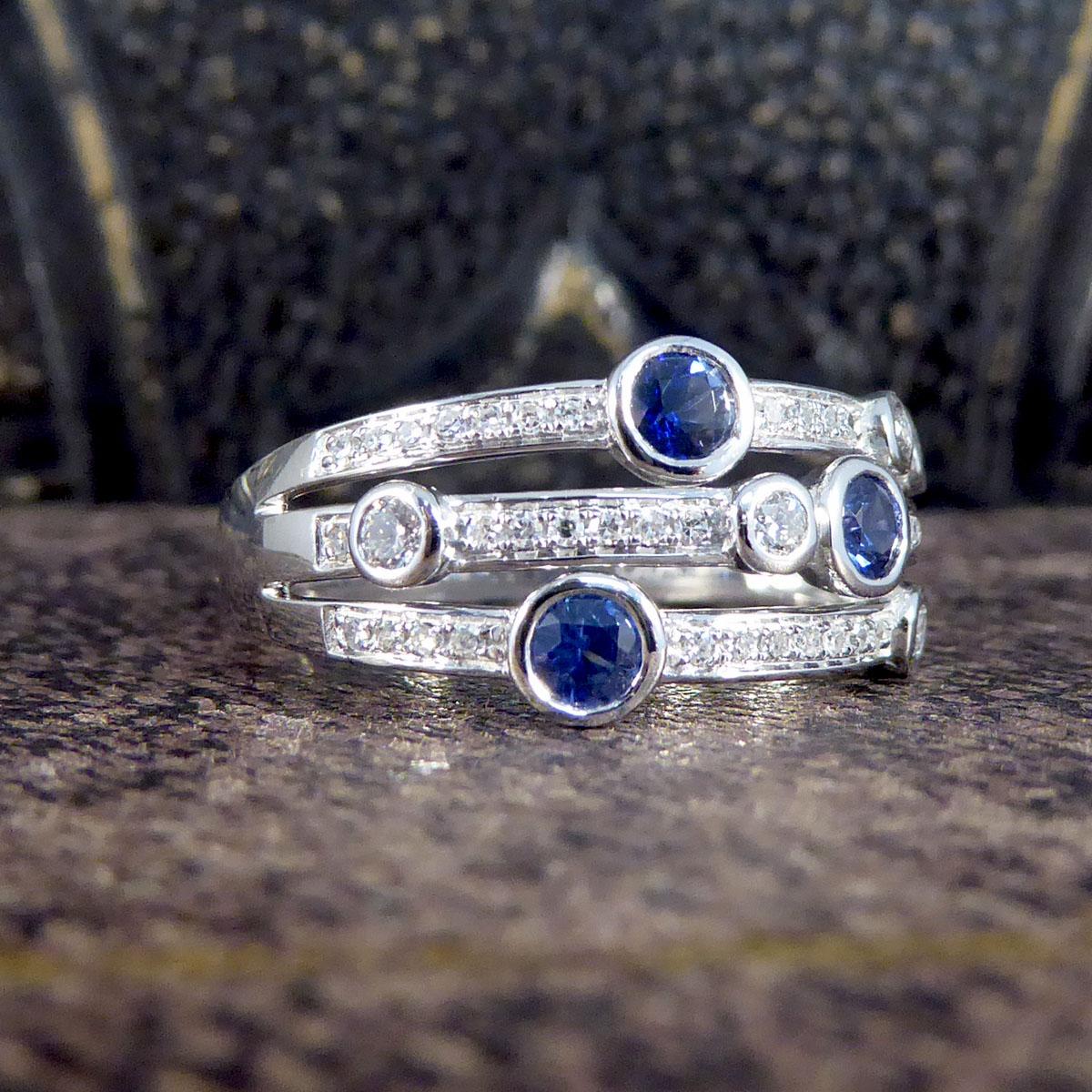 Three strands make up this modern ring, broad in width but elegant in appearance and a brand new ring featuring a combination of Sapphires and Diamonds. Each strand holds a Sapphire in a rub over collar setting with one or two Diamonds mounted the