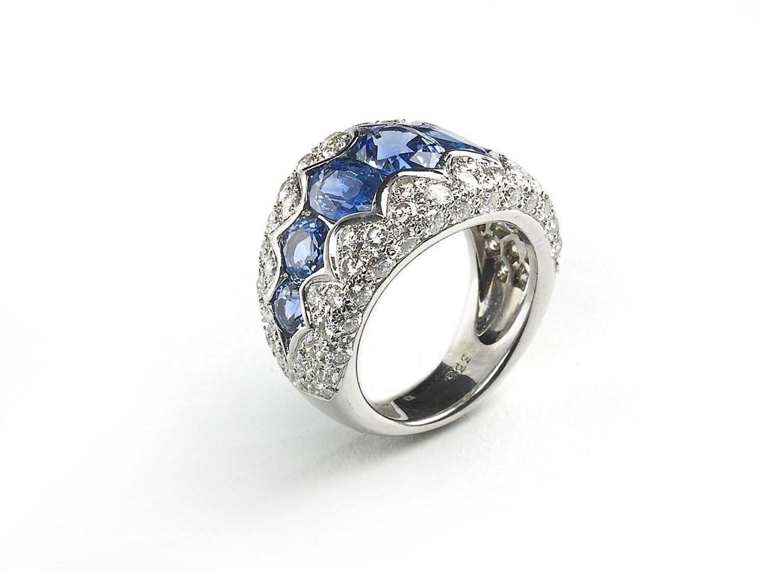 A sapphire and diamond ring, set with a central row of graduating oval and round faceted Ceylon sapphires, with a scalloped edged surround, pavé set with round brilliant-cut diamonds, mounted in 18ct white gold, with a French eagle head mark for