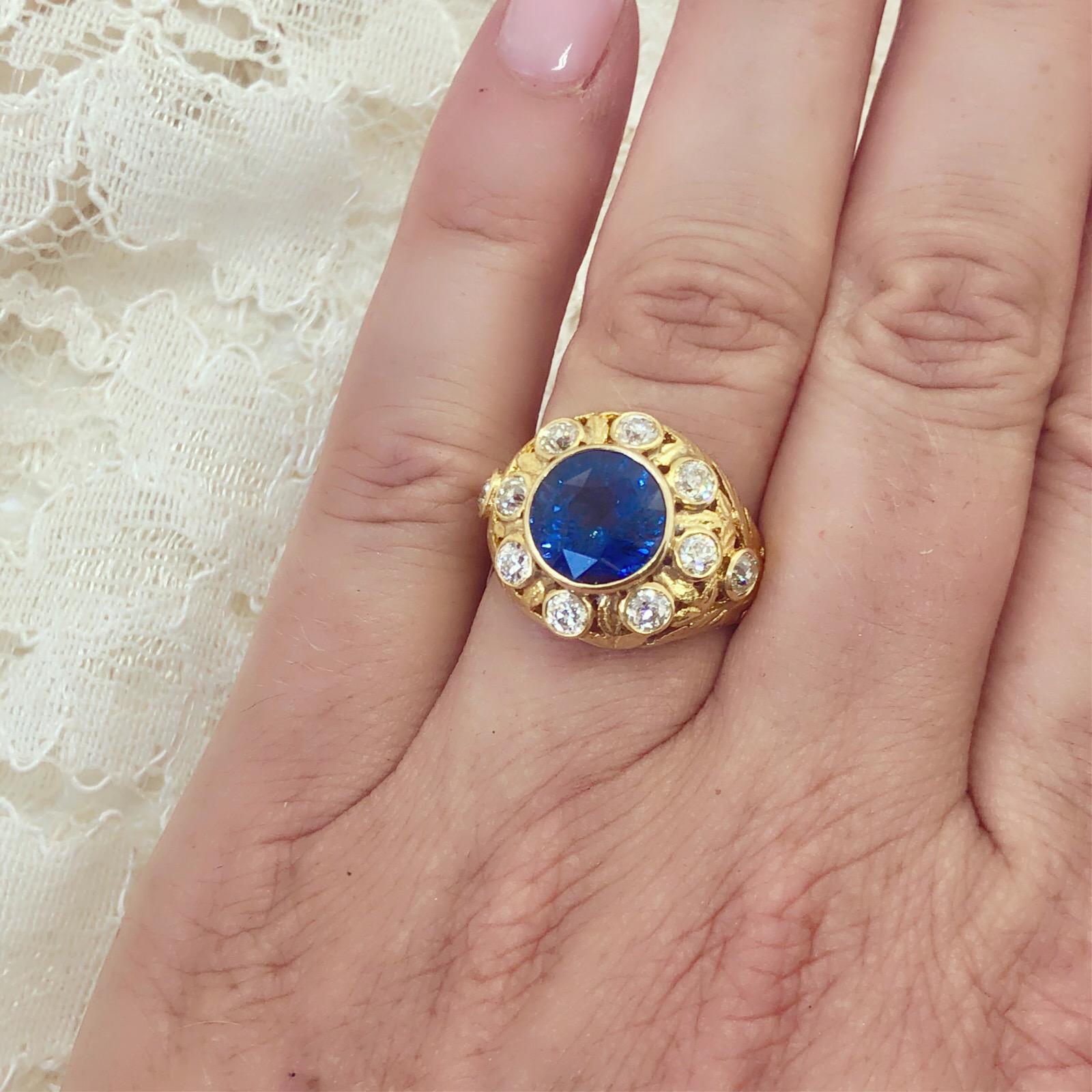 With antique design, this bold 18k yellow gold ring features a round Ceylon sapphire, weighing 4.76-cts, bezel-set and surrounded by 10 bezel-set old mine-cut diamonds, weighing together 0.74-ct. Weighing 7.5 grams and fitting a 7.25 finger size.
