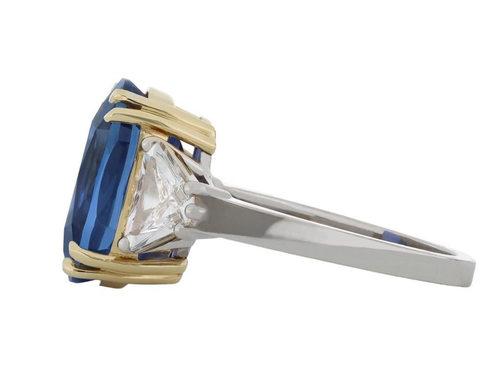 Ceylon sapphire and diamond three stone ring. Set to centre with an oval old cut natural unenhanced Ceylon sapphire in an open back claw setting with a weight of 8.87 carats, flanked by two triangular brilliant cut diamonds in open back claw
