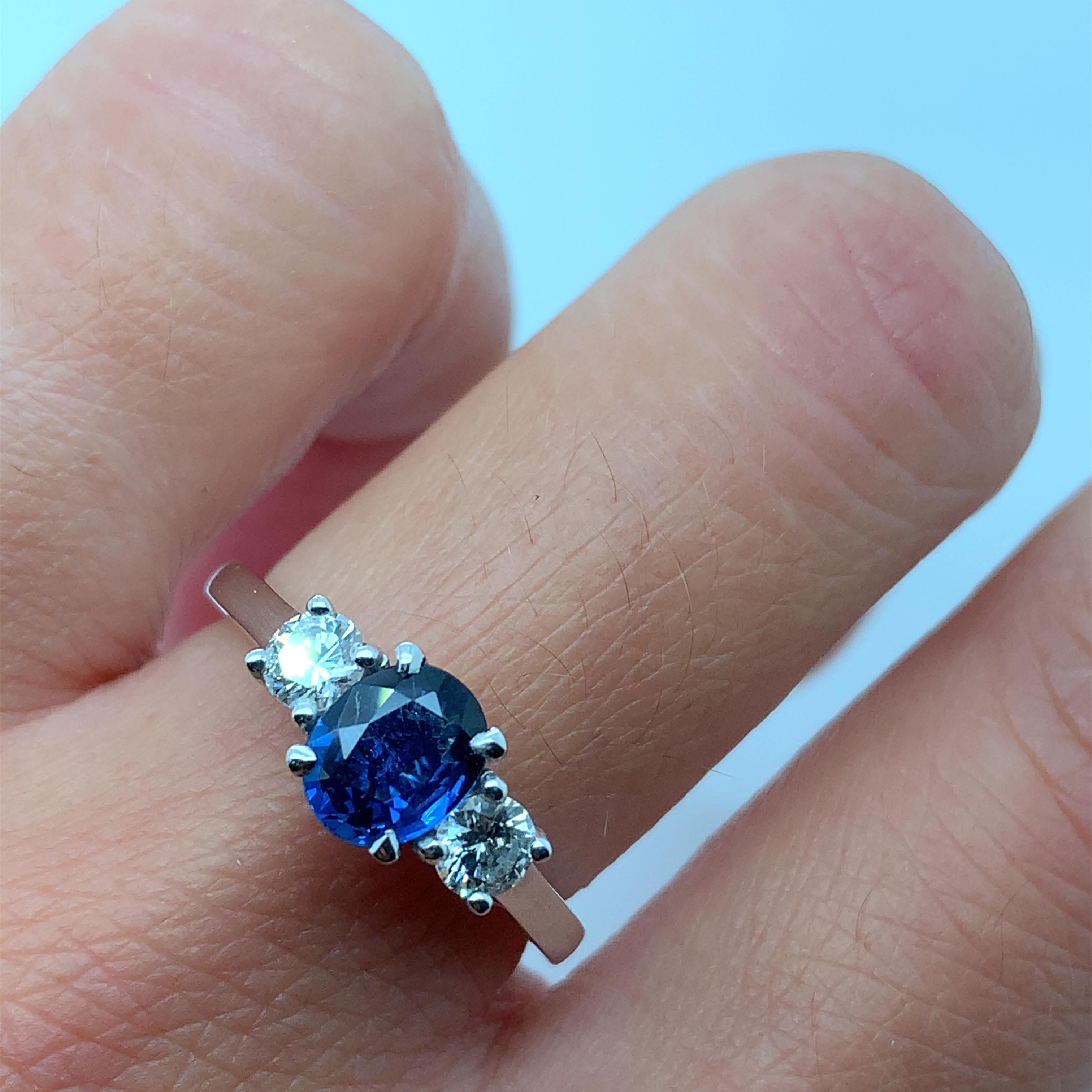 This stunning engagement ring features a natural, oval-shaped blue Ceylon sapphire as its centrepiece, surrounded by two brilliant-cut diamonds on either side. The sapphire has a beautiful blue colour and is not enhanced, while the diamonds have a