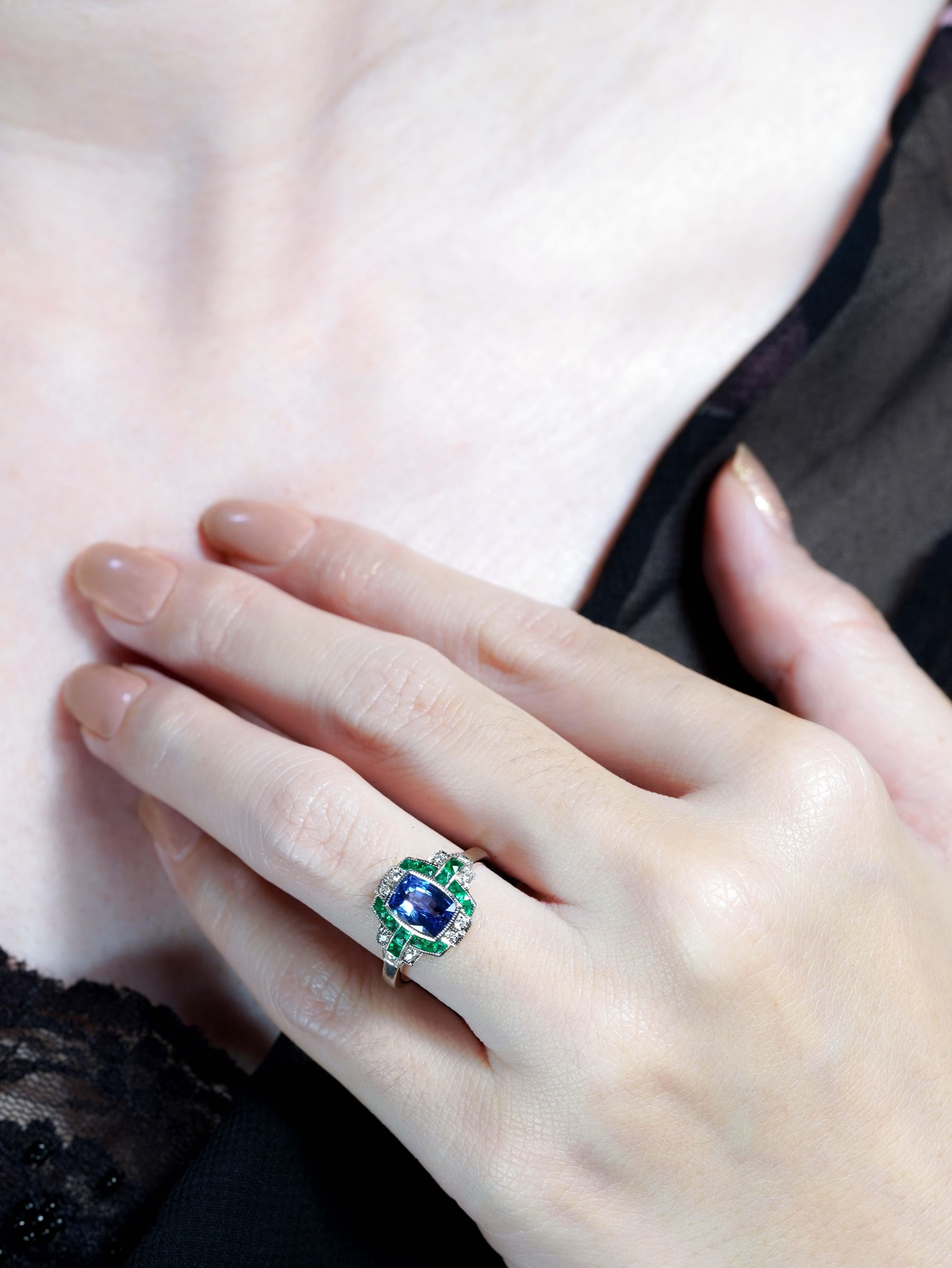 Celebrate timeless elegance with this Ceylon Sapphire, Emerald, and Diamond Art Deco Style Engagement Ring. At its heart lies a vivid cushion shape Ceylon sapphire, renowned for its rich royal blue hue, flanked on each side by vibrant emeralds.