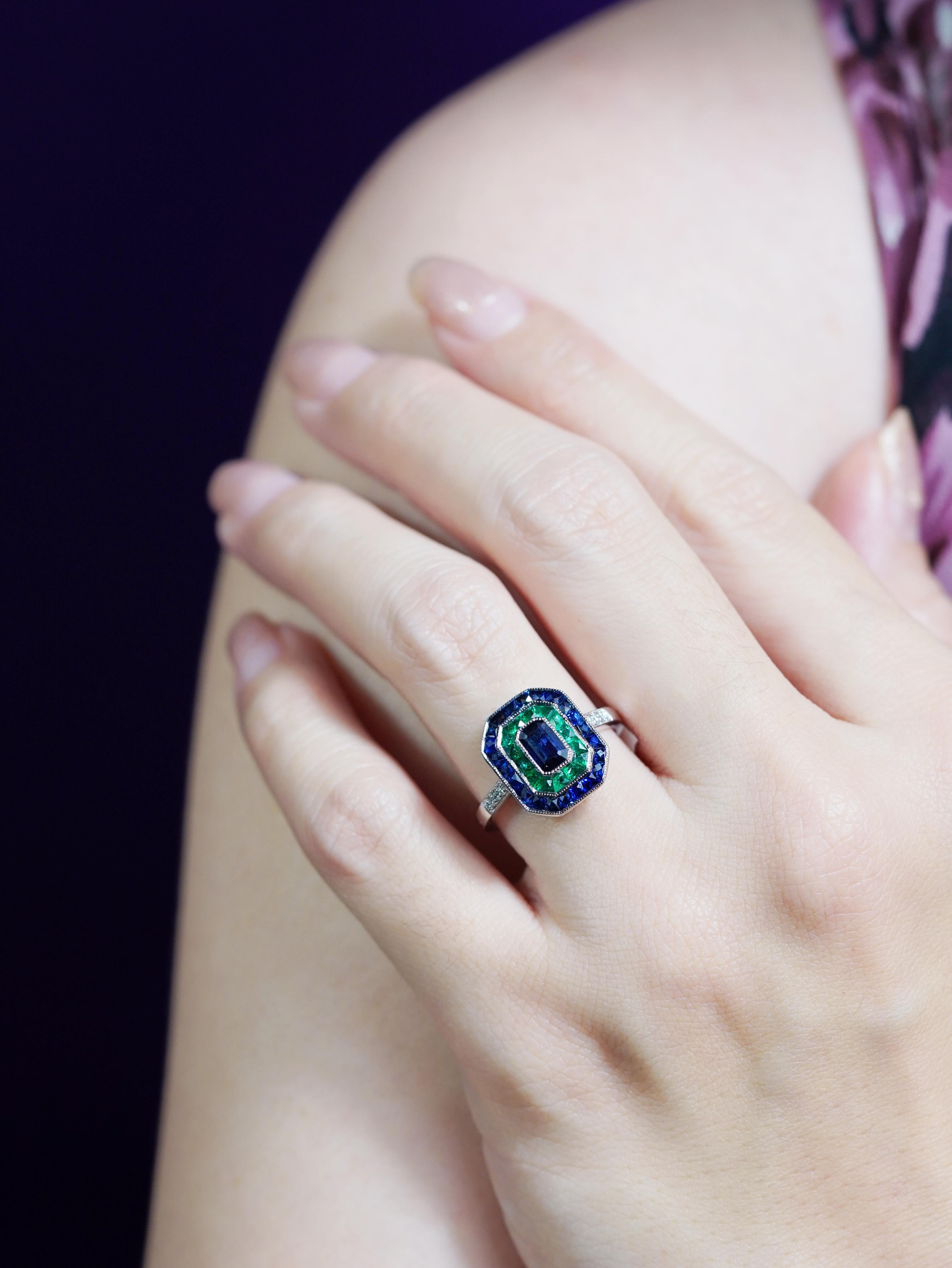 Exuda sofisticación atemporal con este Anillo de Compromiso de Estilo Art Déco, con un zafiro de Ceilán talla esmeralda en su centro. Alrededor del vibrante zafiro azul hay un llamativo segundo halo de esmeraldas talla francesa, que añade un