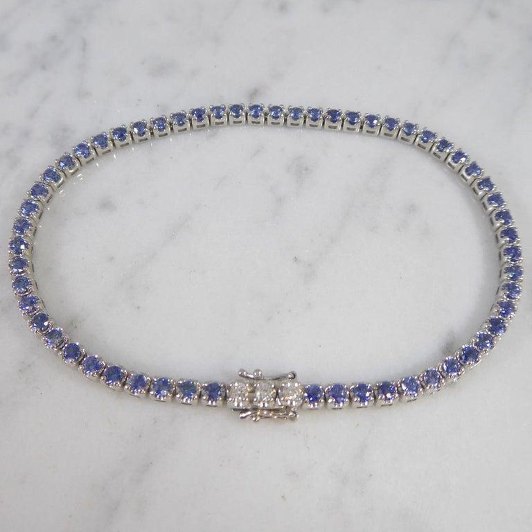 A classic with a difference - a tennis bracelet set with blue sapphires with three brilliant cut diamonds set into the catch.  The sapphires, 58 in total,  are bright and medium blue, and four claw set into individual white gold mounts.  The line