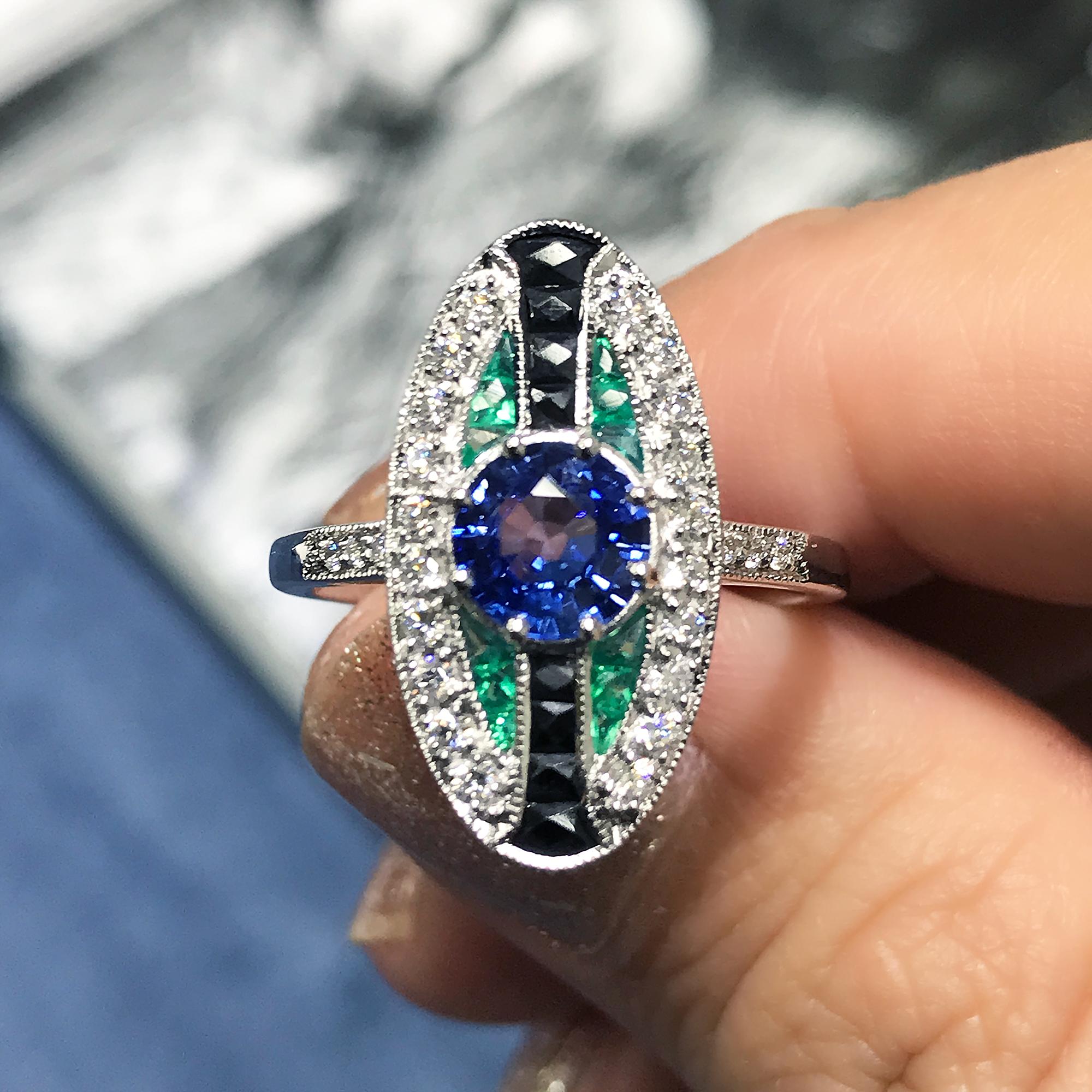 A unique Art Deco style gold ring. It features a vivid Ceylon blue sapphire in the center. On either side are French cut onyx then shaped emerald in a curved design. On the outside and shoulders are well matched white diamonds. There is millgrain
