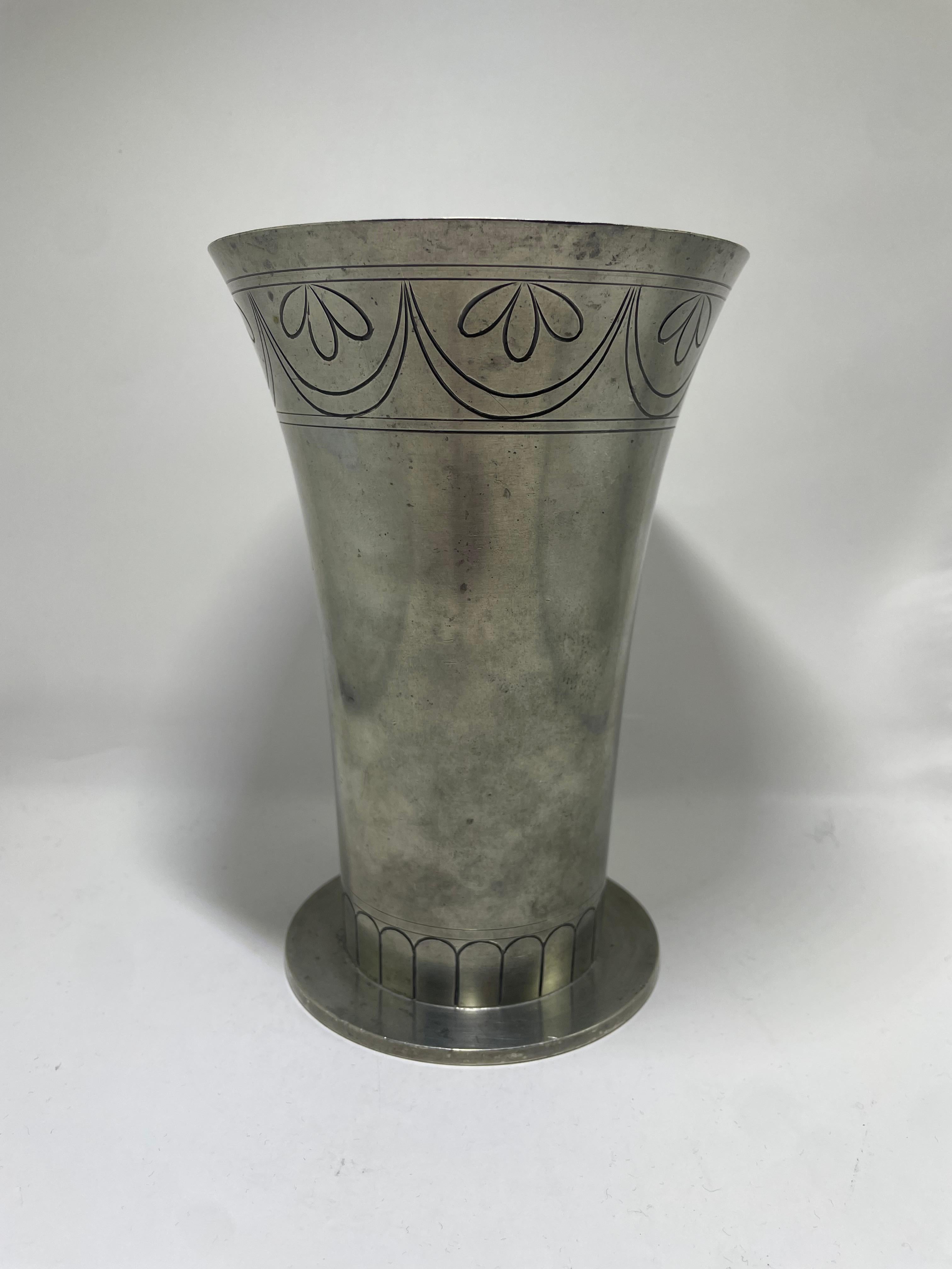Un sorprendente vaso in peltro Art Déco realizzato dai famosi argentieri svedesi CG Hallberg negli anni Trenta. Il vaso presenta un'elegante forma svasata ornata da motivi geometrici e floreali incisi, caratteristici del mix di stilizzazione e