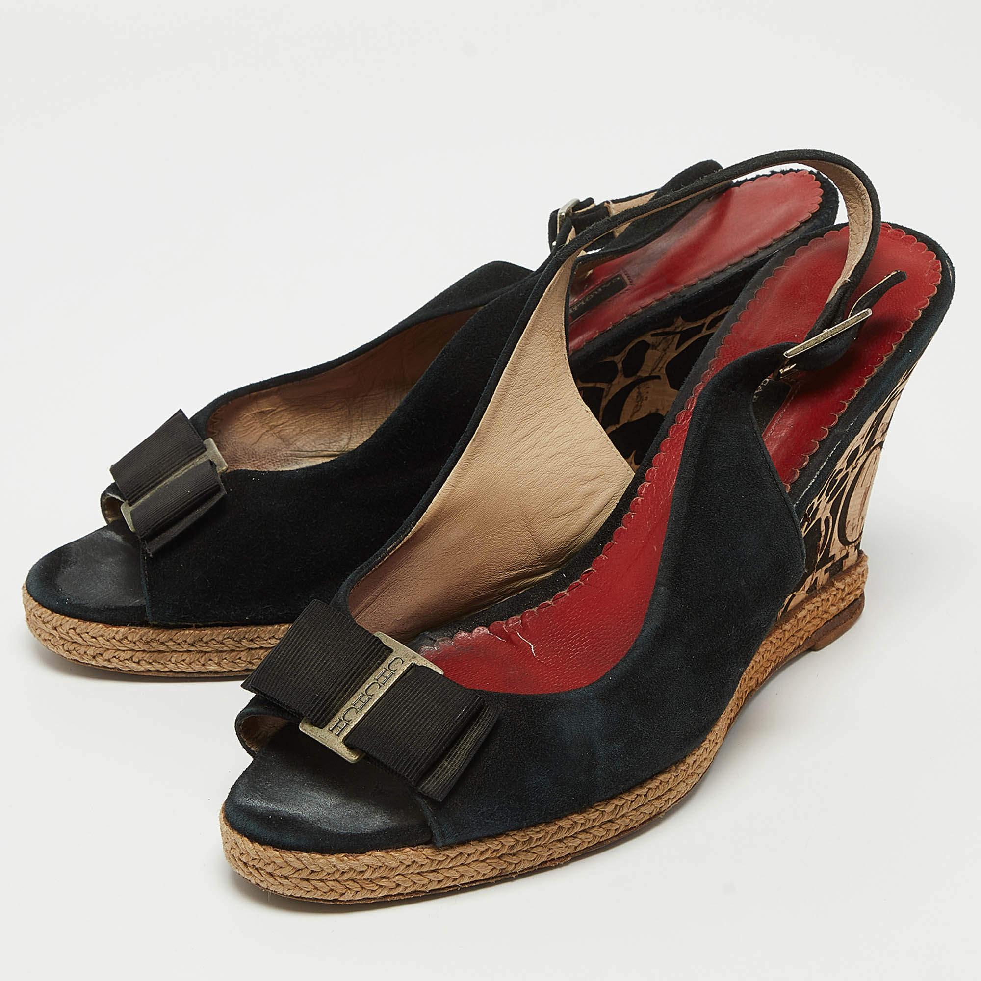Estas preciosas sandalias CH Carolina Herrera te aportarán la dosis justa de estilo y brillo. Están fabricados en ante negro y presentan detalles de logotipos en tono plateado en la parte delantera y tacones de cuña de corcho de 9 cm. Son bonitas y