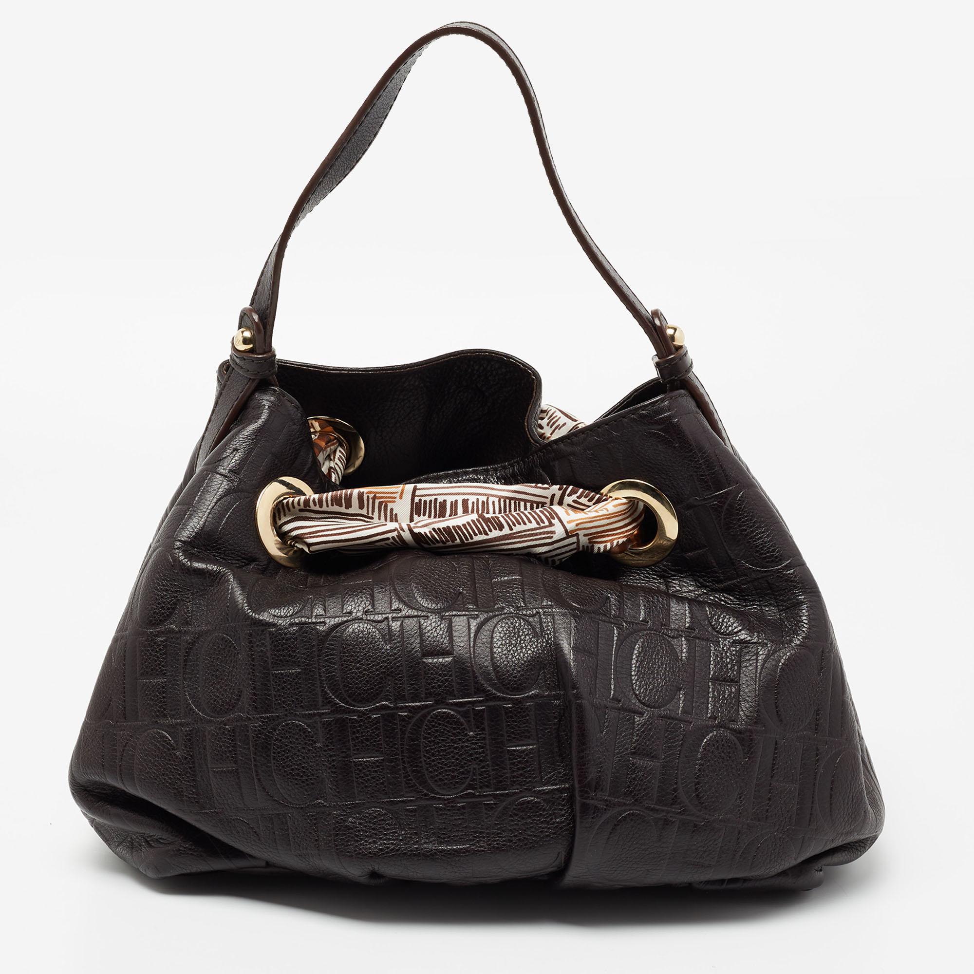 This CH Carolina Herrera hobo is great for everyday use. Crafted from Monogram embossed leather, this dark brown hobo is handy and stylish with a signature appeal. It has a single handle, a fabric interior, scarf detailing, and gold-tone