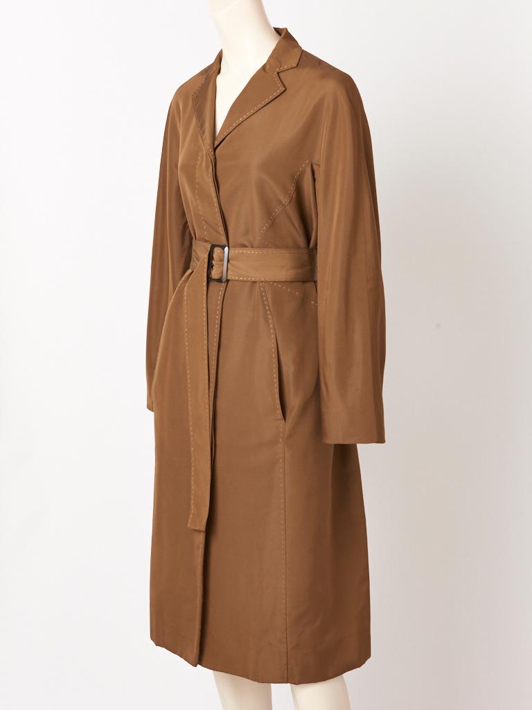 Chado Ralph Rucci, taffeta faille, bronze tone, belted coat, having a small lapel collar, hidden button closures, (buttons are tortoise) a double vent at the back, slash pockets, and contrasting, signature, top stitching detail throughout. Coat is