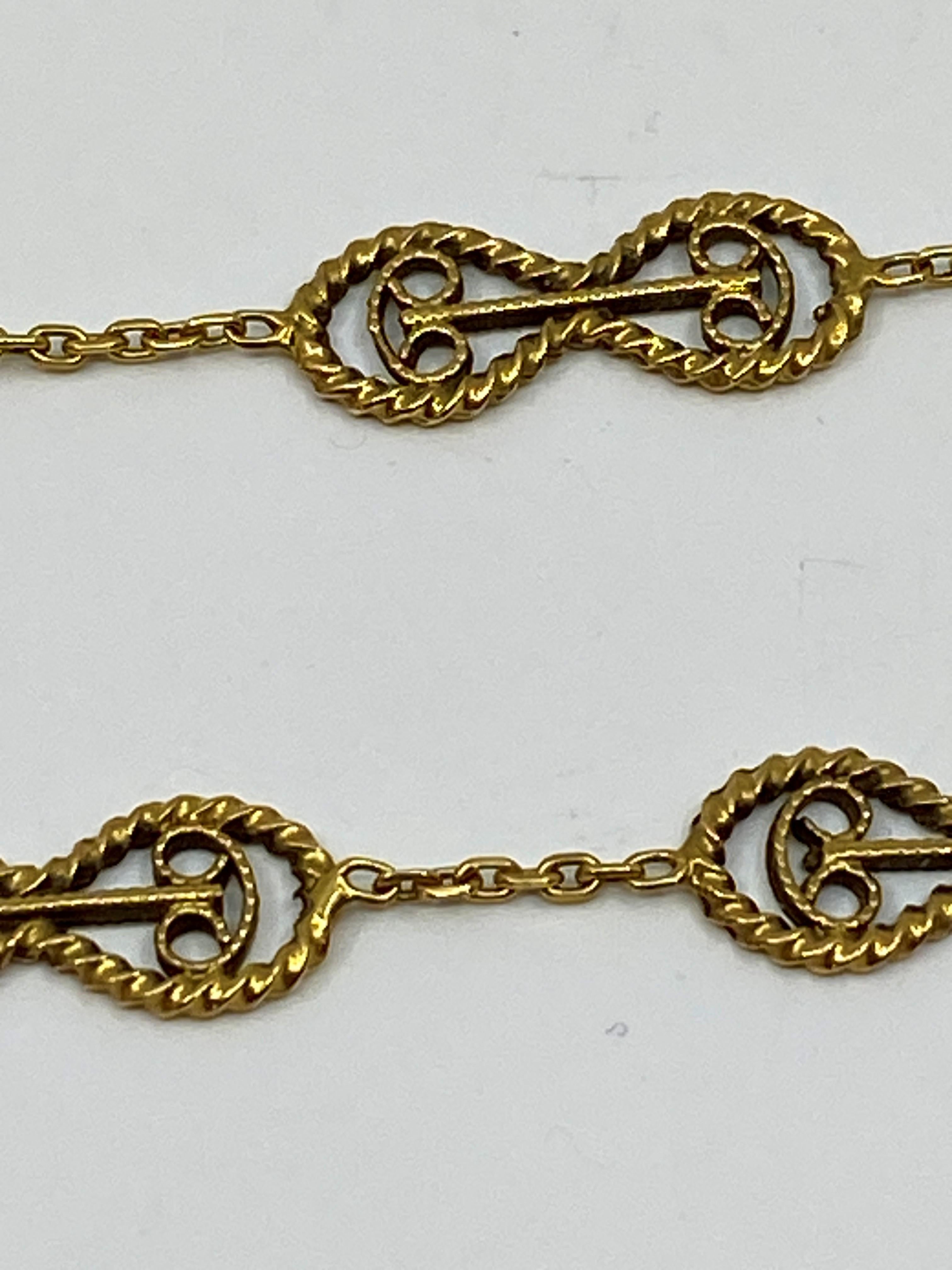 Ravissante chaîne en or 18 carats, elle est constituée de mailles en forme de huit décorées de motifs en filigrane. Ces motifs sont reliés entre eux par une chaîne forçat. Cette chaîne est terminée par un fermoir à ressort. La rareté du modèle de ce
