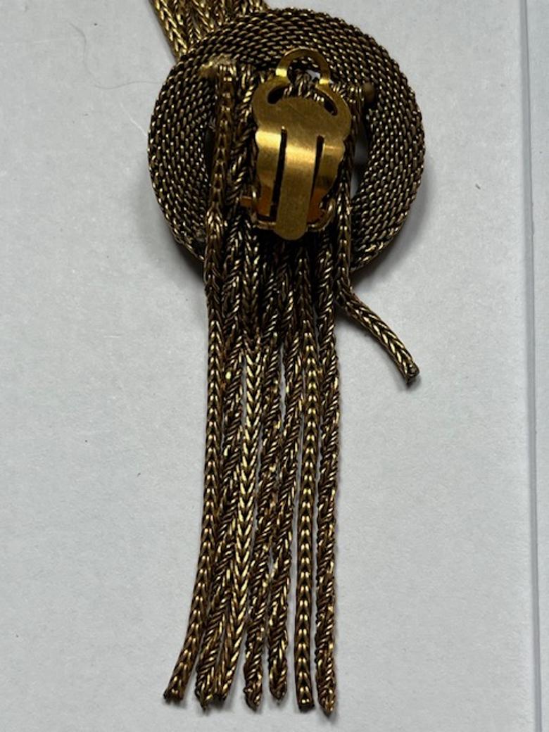 Questo sorprendente paio di orecchini a clip presenta un'intricata catena a spirale alla base, da cui scende un mix di catene intrecciate e ritorte in ricche tonalità dorate e annerite. Il gioco dinamico di texture e colori crea un movimento