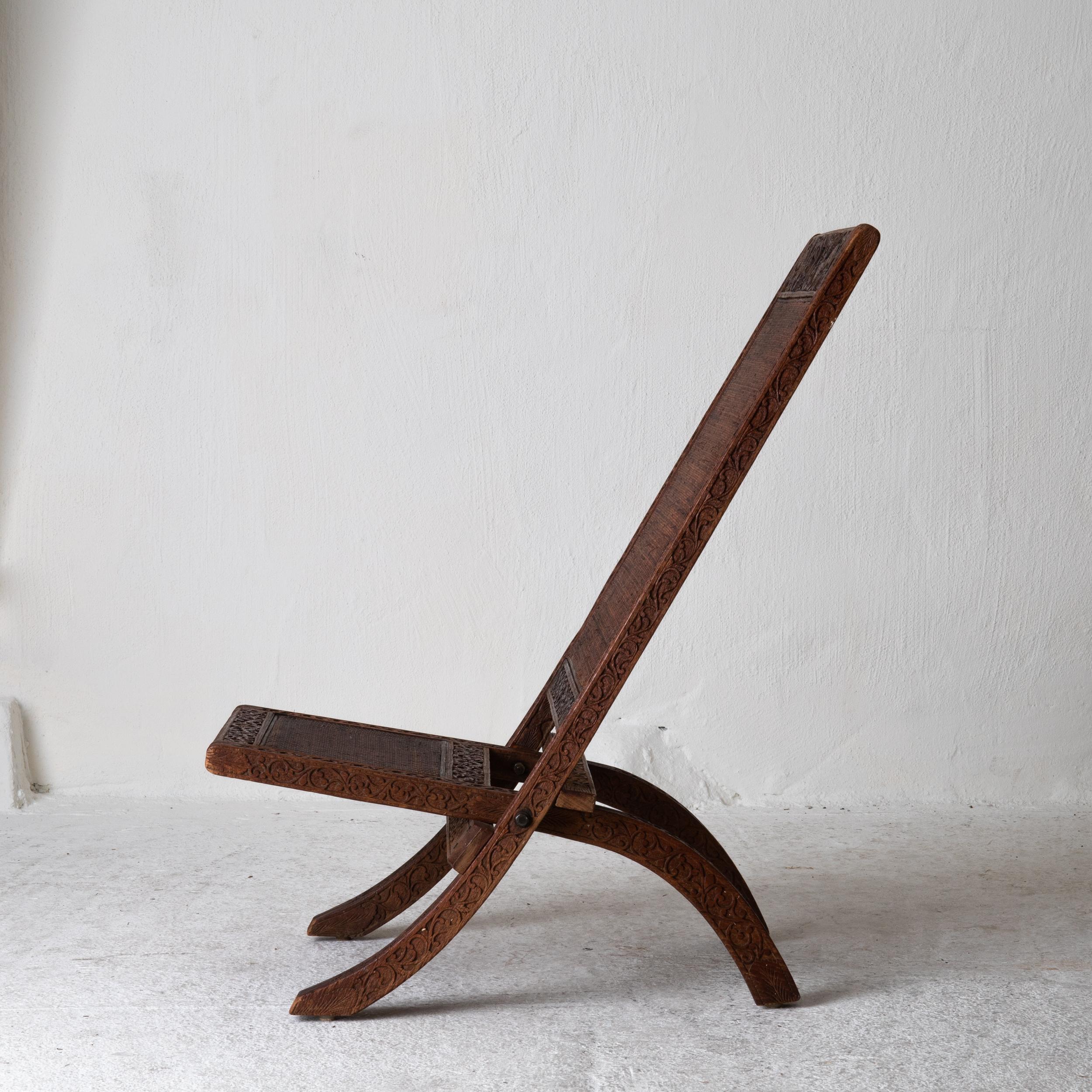 Stuhl faltbar Indien braun geschnitzt, 20. Jahrhundert, Indien. Ein klappbarer Stuhl, der zu Beginn des 20. Jahrhunderts in Indien hergestellt wurde. Geschnitzter Rahmen mit Elefanten, Vögeln und Blättern verziert. 

 