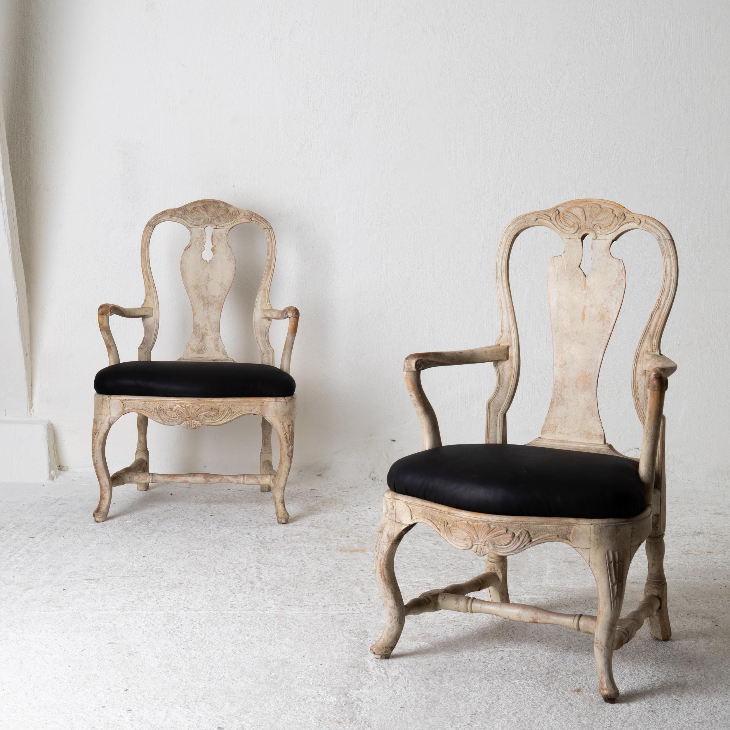 Chairs armchairs pair Swedish Rococo 1750-1775 cream white, Sweden. A pair of armchairs made during the Rococo period 1750-1775 in Sweden. Restored in a light creamy white paint. Seat upholstered in black leather. Back and frieze carved with a shell
