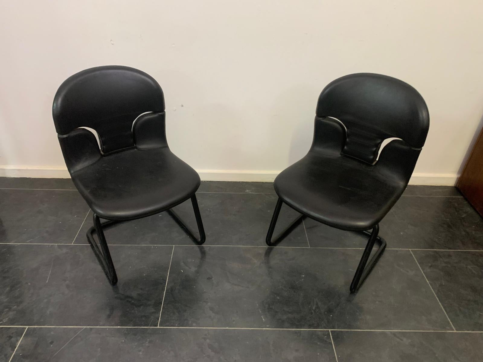 A pair of armchairs with suspended seats, featuring a painted metal base and upholstered backrest and seat covered in black leather. 
Light wear due to age and use, in overall good condition, solid and functional.