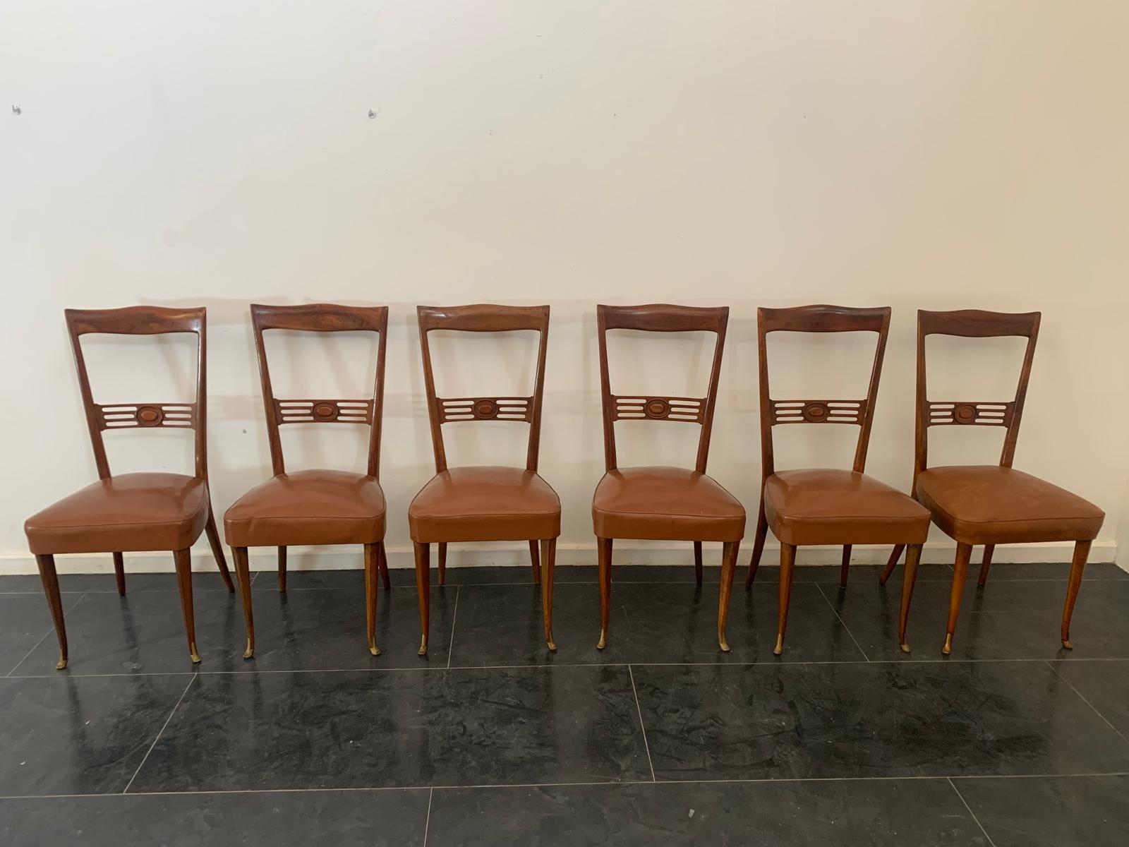 Eccellente lavorazione del mobile per queste 6 sedie in palissandro massiccio. Le due gambe anteriori sono rifinite a sciabola e terminano con punte feline in bronzo dorato, mentre lo schienale si snoda al centro con tre linee parallele che ospitano