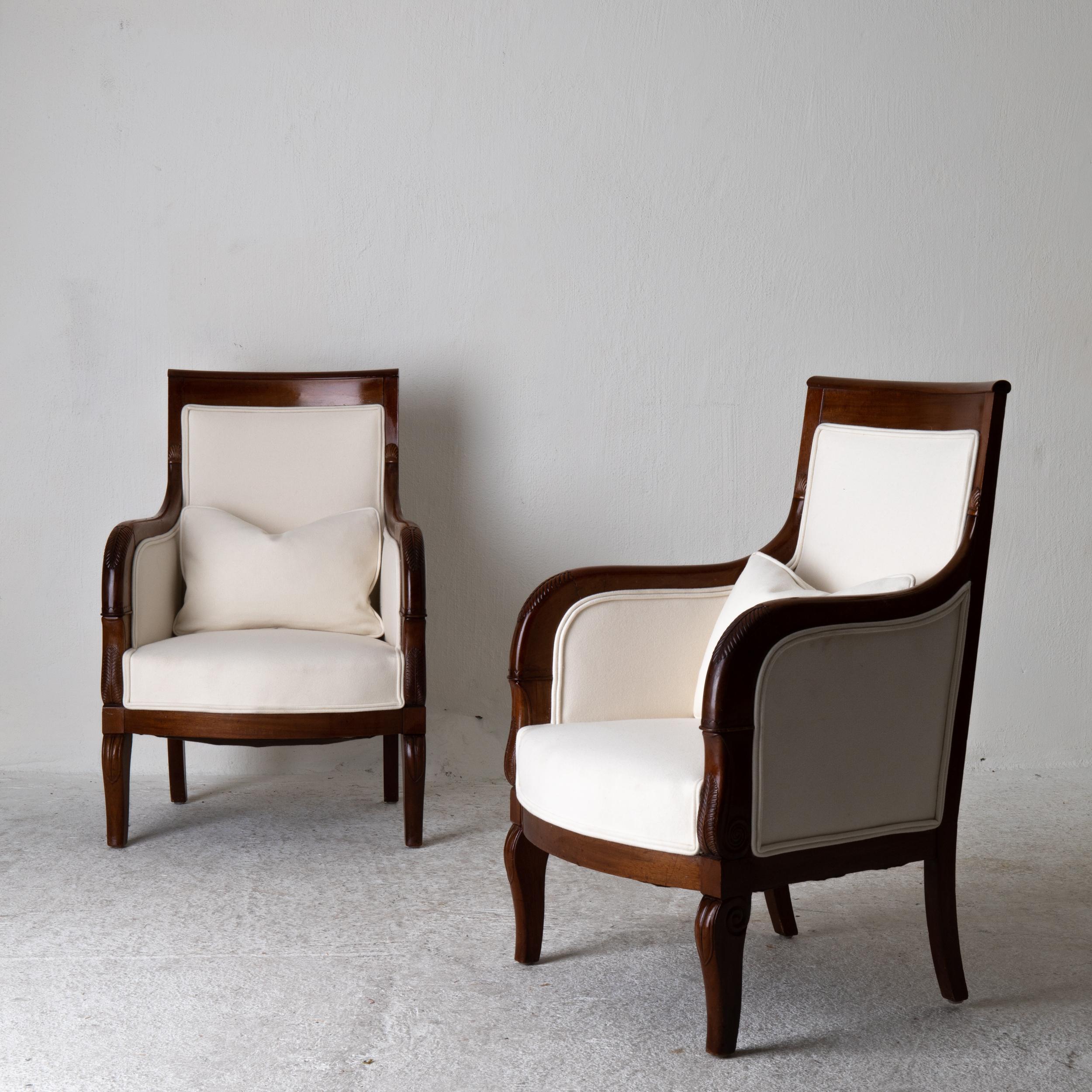 Chairs pair of Bergeres 19th century Directoire French mahogany white, France. A pair of lounge chairs made in France during the early 19th century. Frame in mahogany. Upholstered in a cream white wool fabric. Loose decorative cushion.