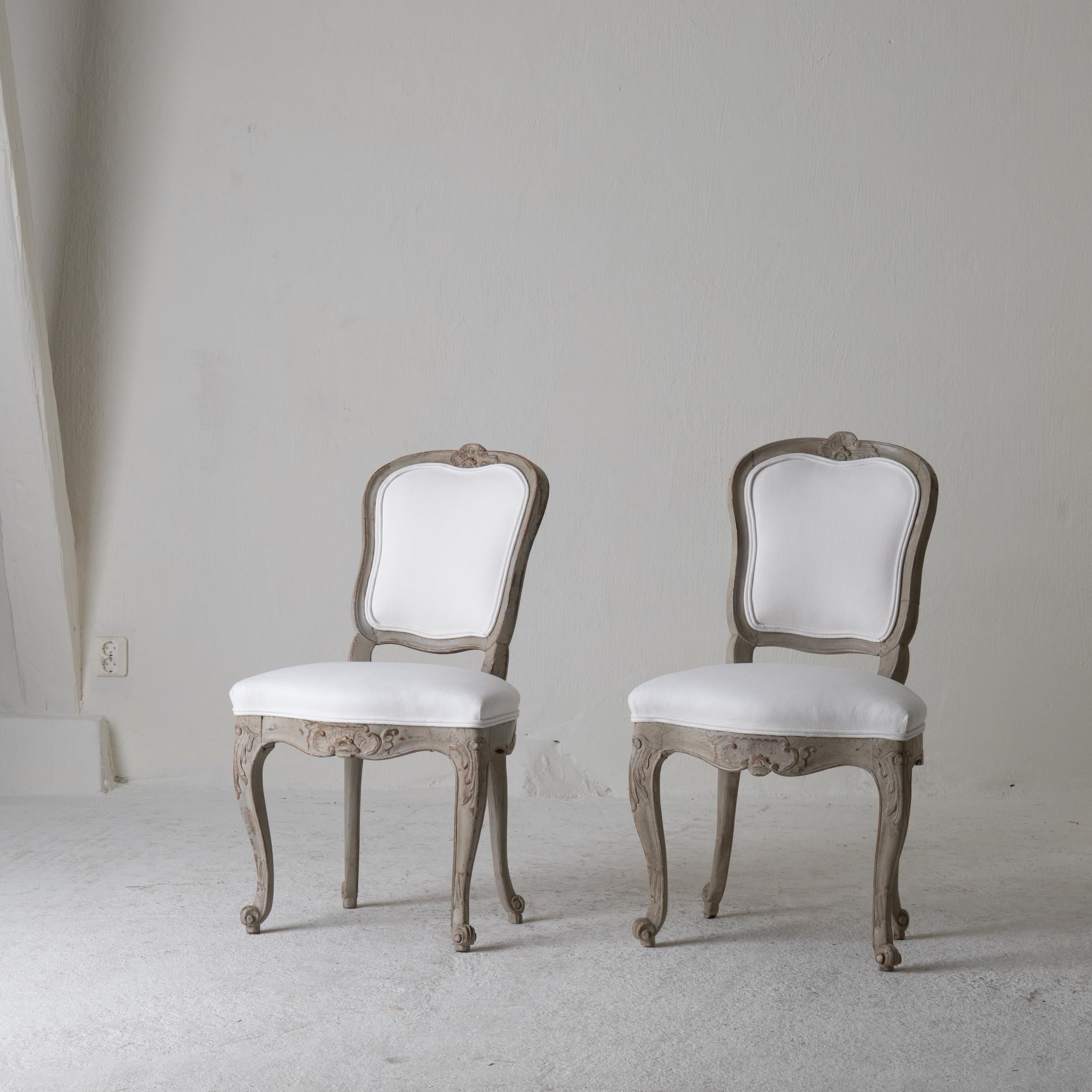 Paire de chaises suédoises Rococo 1750-1775 blanc vert gris, Suède. Une paire de chaises d'appoint fabriquées pendant la période rococo 1750-1775 en Suède. Peint dans un gris verdâtre et tapissé d'un doux tissu de coton blanc. Détails sculptés de