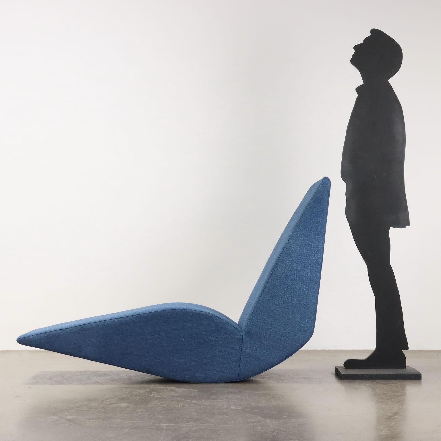 Rocking seat with a sculptural, monolithic form with a wood and metal frame, differentiated density foam padding and freshly reupholstered blue fabric cover.