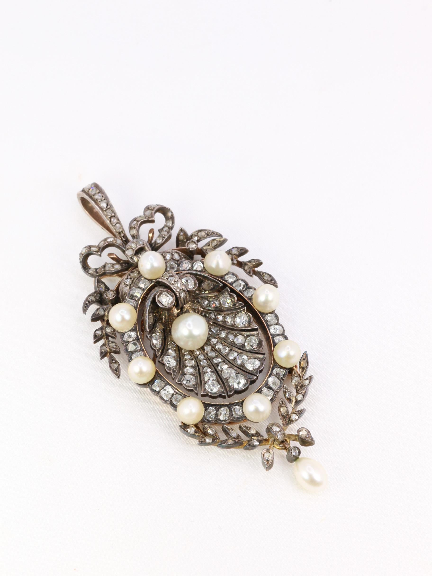 Oval pendant-brooch in 18k (750°/°°) gold, silver and natural pearls featuring a shell. 
The centerpiece is set with a 6.5 mm calibrated mobile button pearl and falling old mine cut and rose-cut diamonds. The shell-shaped central motif is surrounded