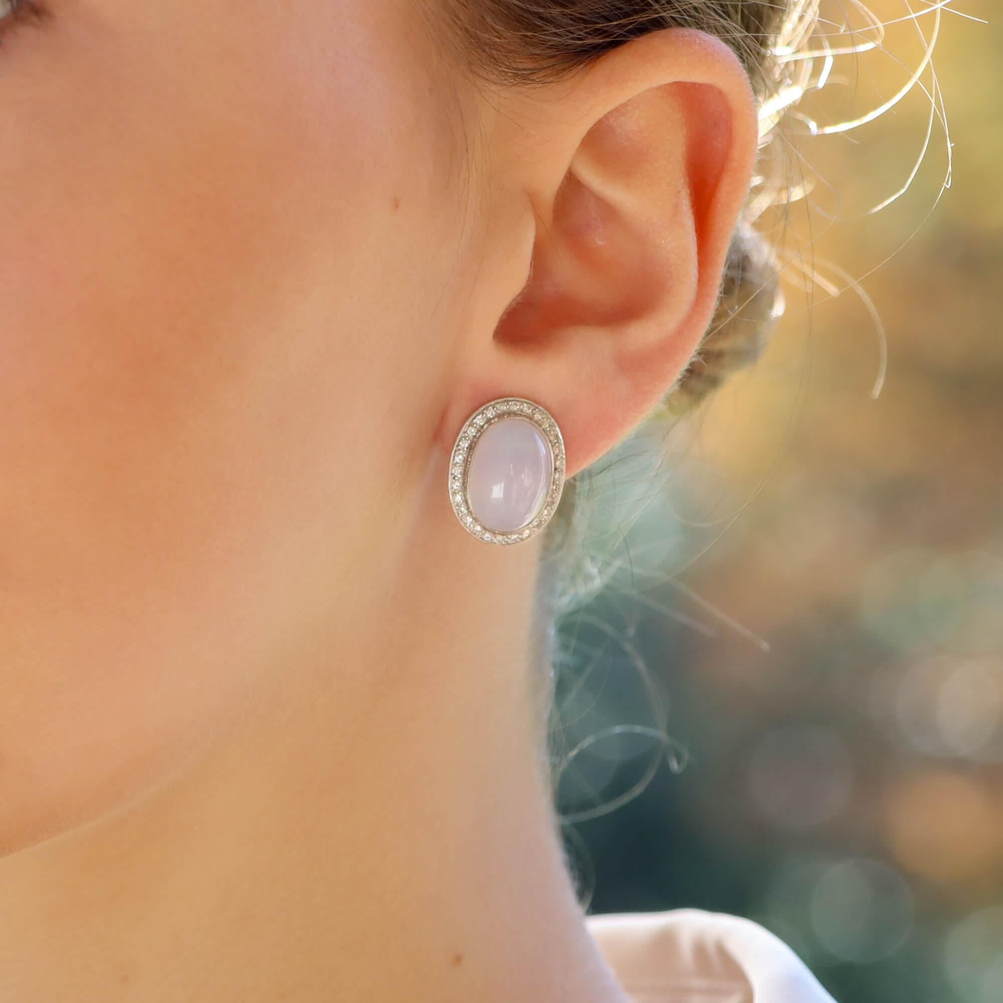 A beautiful pair of rub over set oval blue/grey Chalcedony earrings surrounded with round brilliant cut diamonds. The diamonds are grain set in 18ct white gold and secured with a post and clip fitting. 

Total diamond weight is approximately