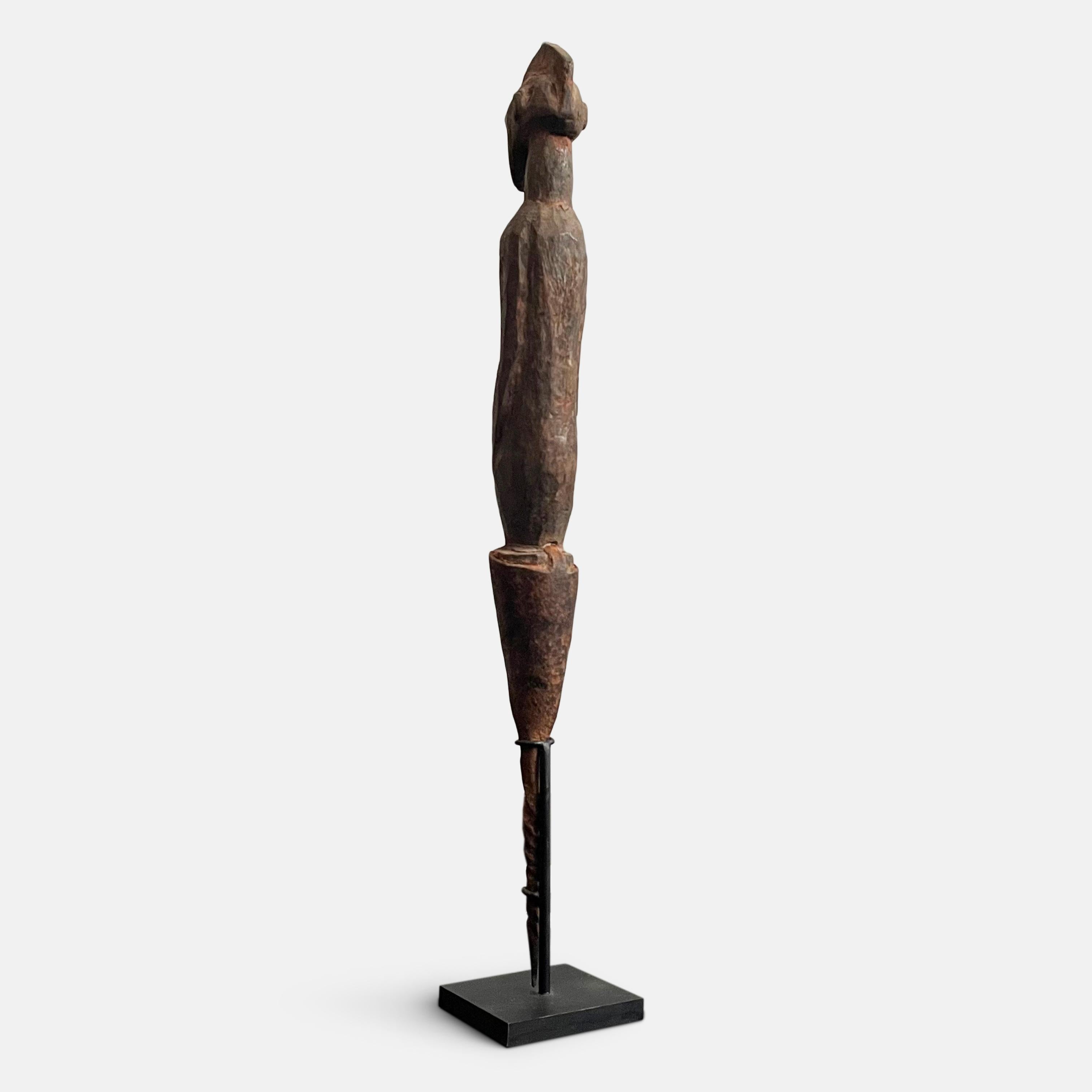 A small columnar, spiked statue in the form of a male figure, known as a ‘Tau-Wandoa’ (female statues are known as ‘Tau-Kendoa’), made from hard wood and a crafted iron stake allowing it to be driven into the ground. Made by the Chamba people to the