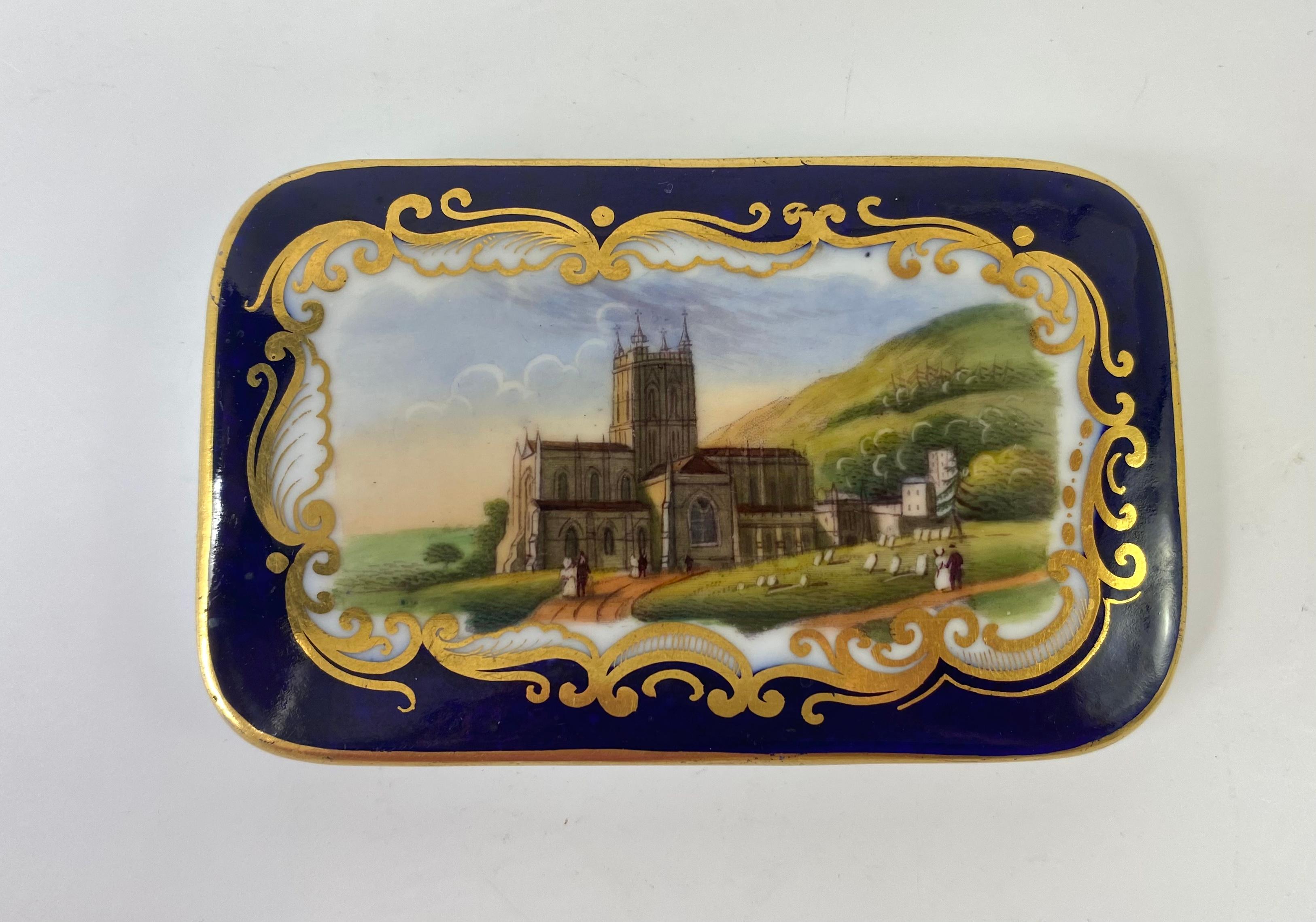 Chamberlain Worcester porcelain box and cover, c. 1840. The cover painted with a titled view of ‘Malvern’, of figures before the church, beneath the hills, within a gilt scroll framed panels, on an underglaze cobalt blue ground.
The base in cobalt